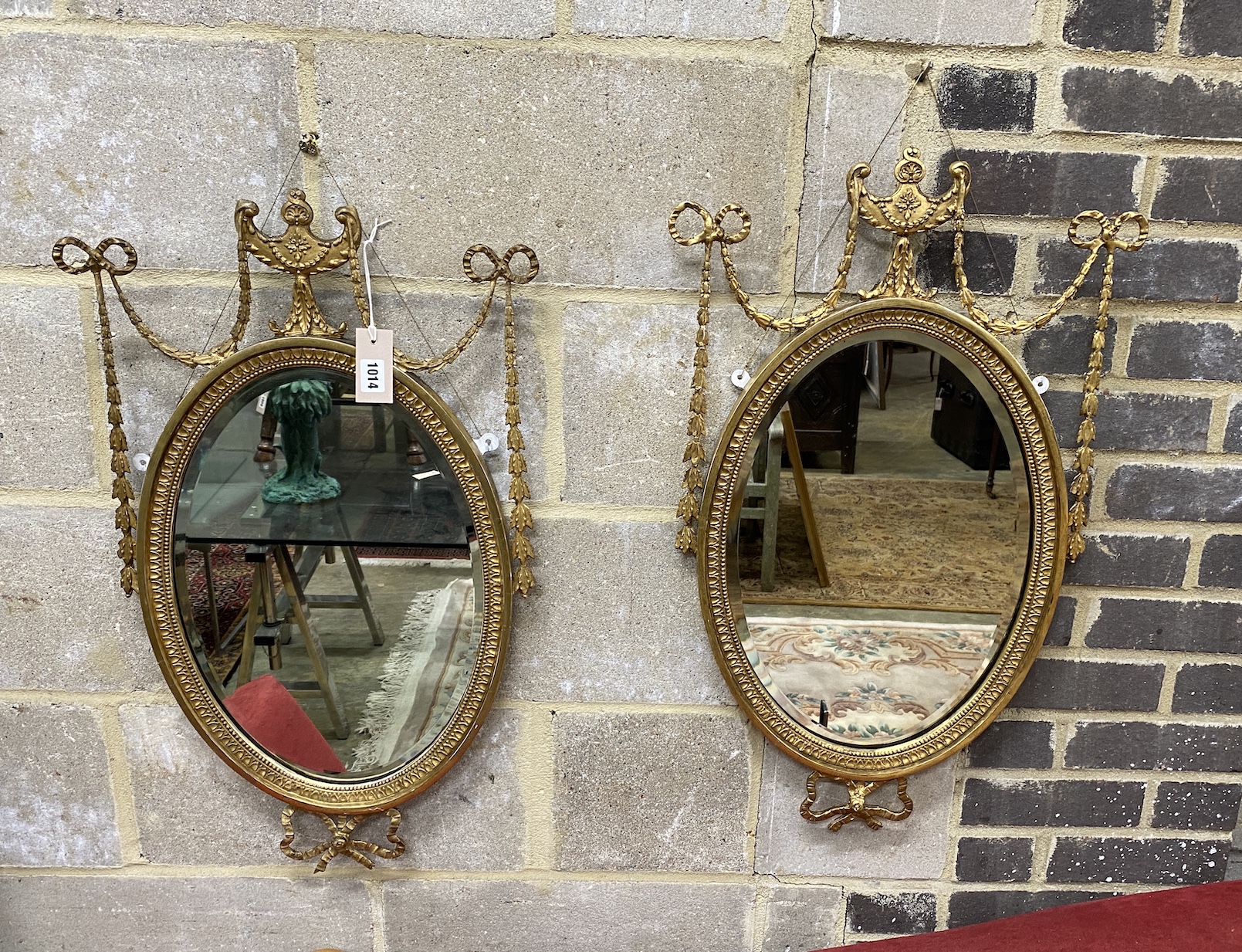 A pair of Edwardian Adam design giltwood and composition oval wall mirrors with swagged urn pediments, width 42cm, height 74cm                                                                                              