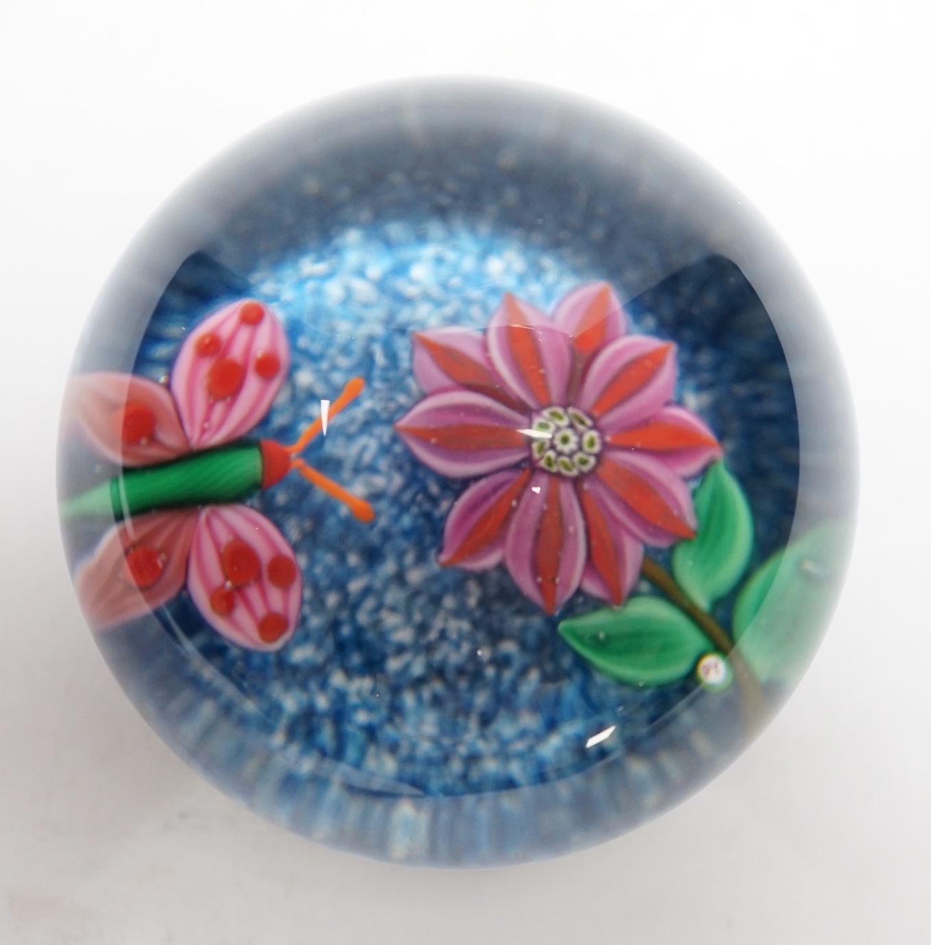 A rare Paul Ysart ‘insect and flower’ footed glass paperweight, Caithness period, scratched signature ‘P. Ysart’, ‘PY’ cane, decorated with a butterfly and pink dahlia, blue jasper ground, raised on a dark green glass fo