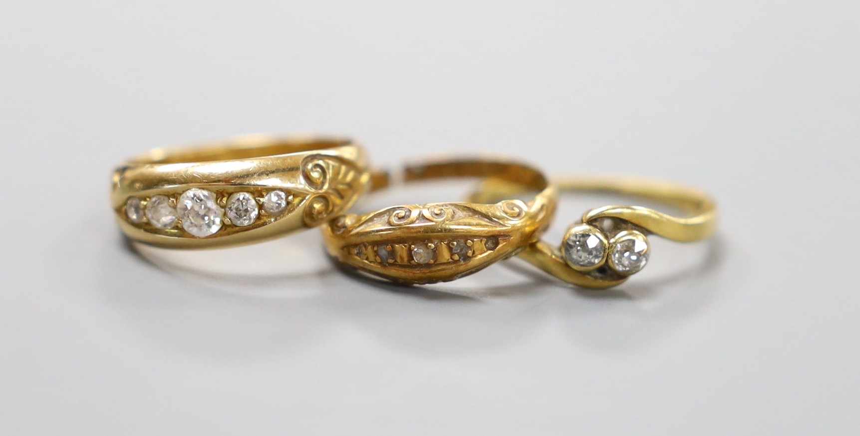 A late Victorian 18ct gold and graduated five stone diamond set half hoop ring, size M/N, a George V 18ct gold and diamond chip set ring (shank cut), gross 6.8 grams and a yellow metal and two stone diamond set crossover