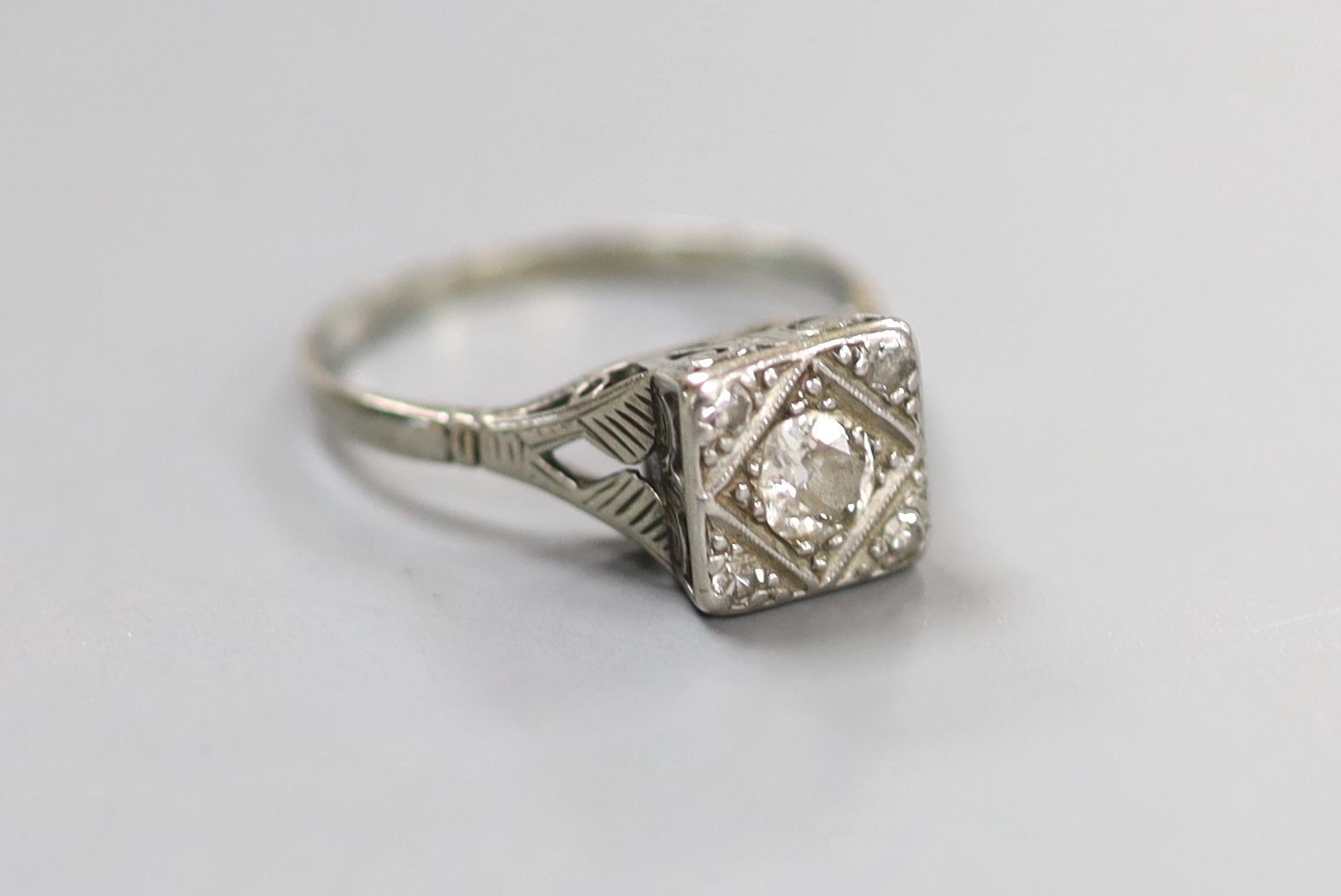 A 1920's/1930's white metal and single stone round cut diamond set square ring, with diamond set corners, size O/P, gross weight 2.9 grams.                                                                                 