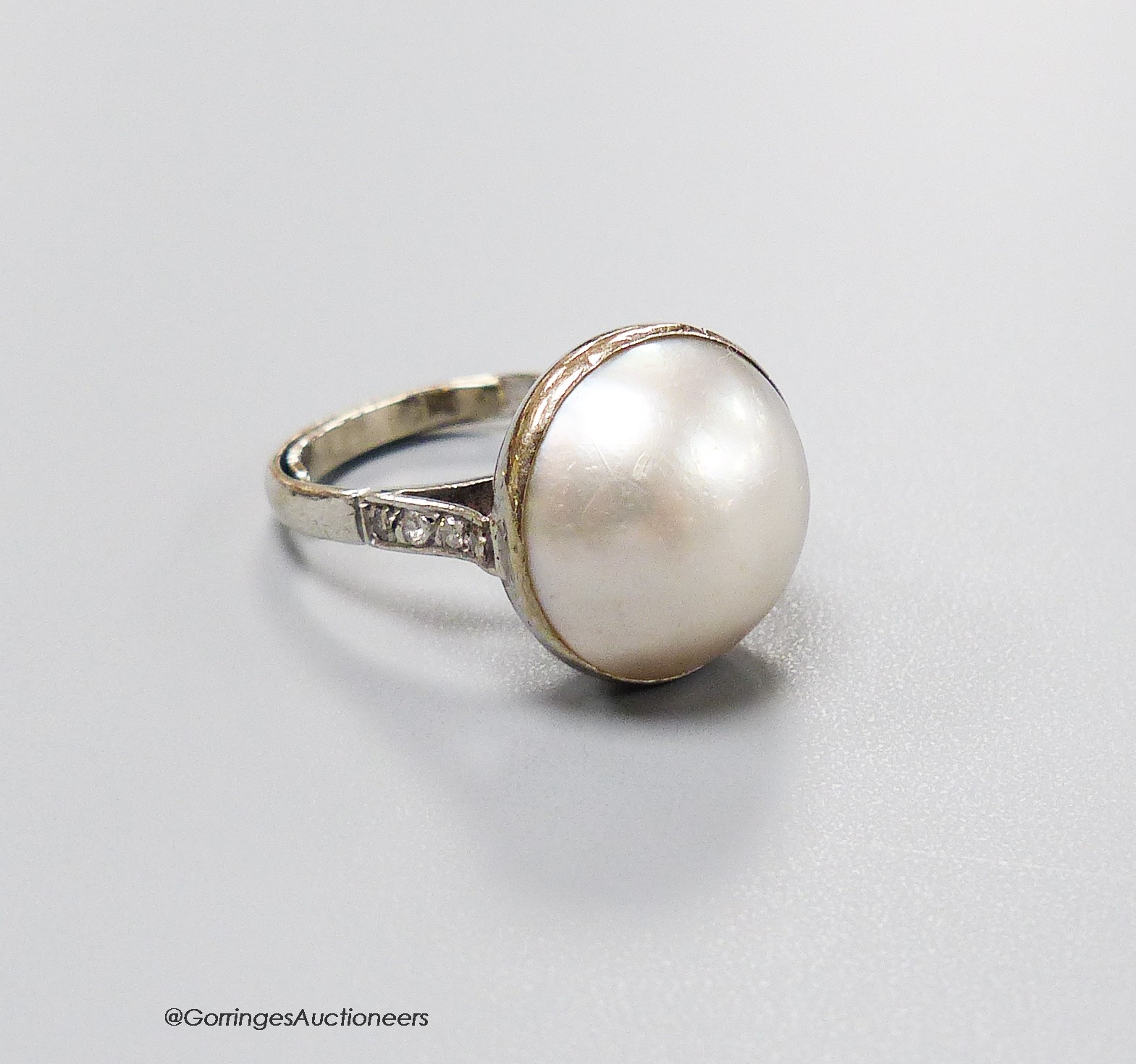 An 18ct white metal and mabe pearl set dress ring with diamond set shoulders, size N, gross 7.2 grams.                                                                                                                      