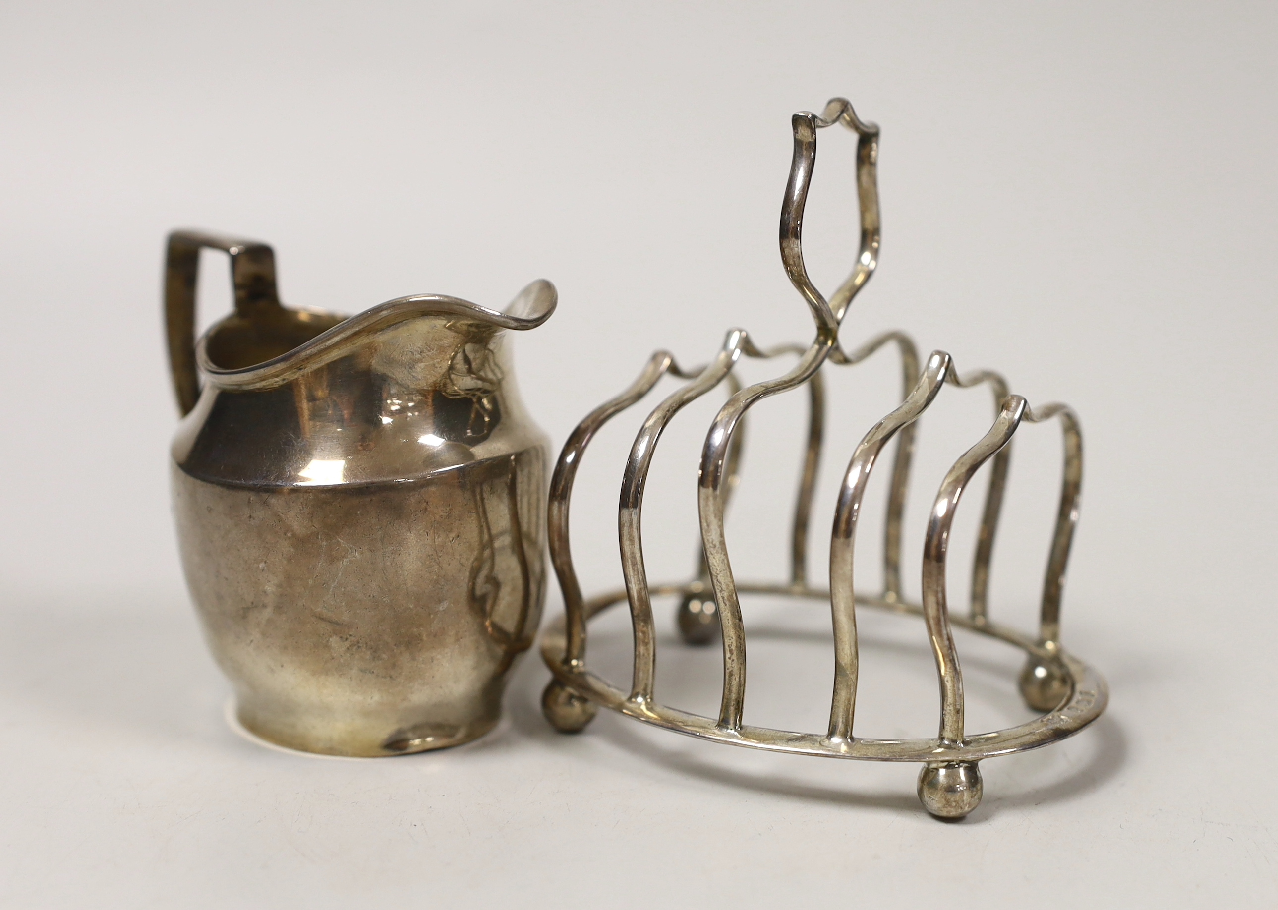 An Edwardian small silver five bar toast rack, Birmingham, 1906, length 94mm and a later silver ceam jug by George Unite, 5.1oz.                                                                                            