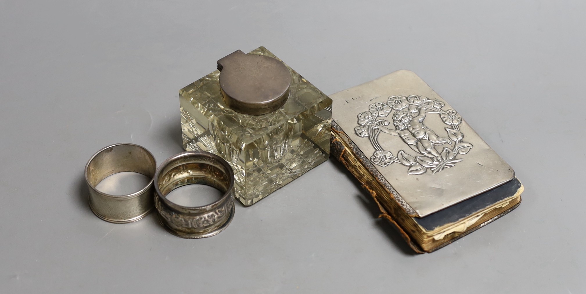 A George V silver mounted cut glass inkwell by William Hutton & Sons, Sheffield, 1910, width 67mm, two silver napkin rings and a silver mounted book of Common Prayer.                                                      