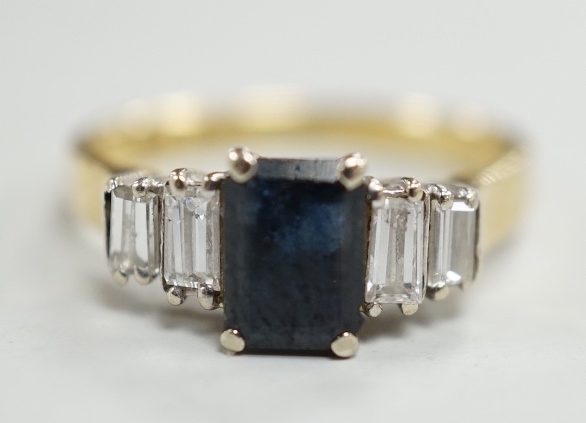 A modern 18ct gold and single stone emerald cut sapphire set ring, with graduated baguette cut diamond set shoulders, size J/K, gross weight 3.1 grams.                                                                     