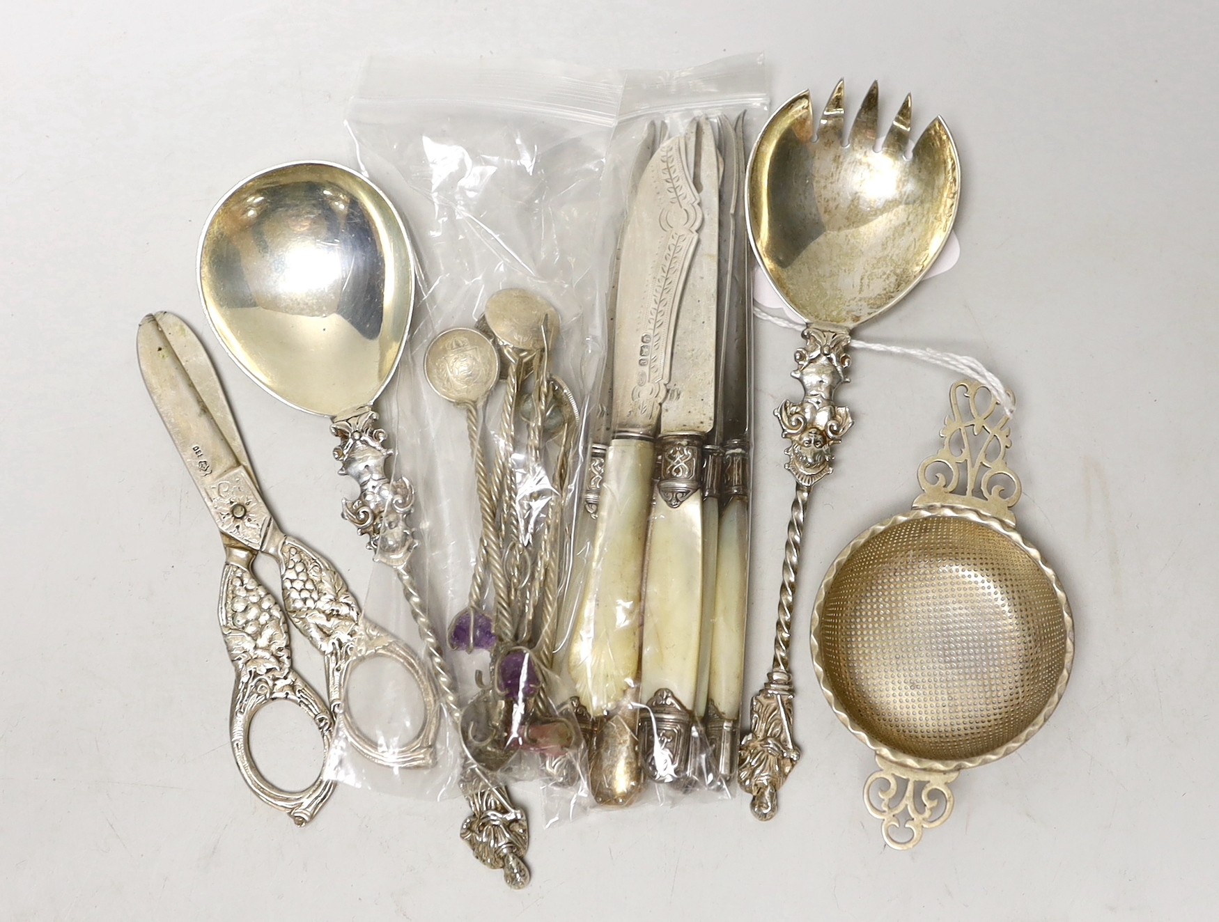Small silver including a pair of late Victorian servers, by William Hutton & Sons, 830 standard white metal grape shears, tea strainer, fruit knives and novelty coin spoons and forks.                                     