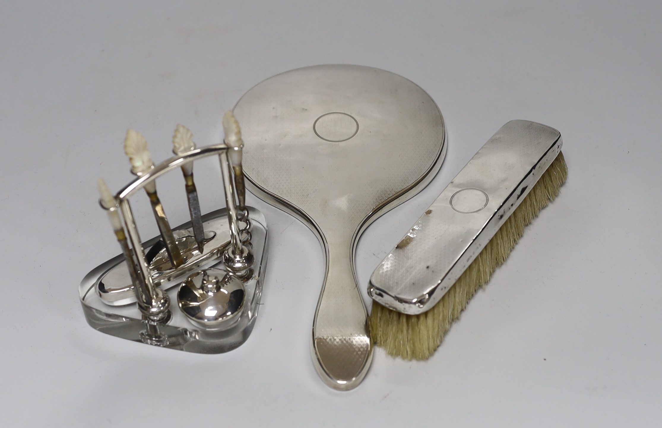 A George V silver mounted glass manicure stand with six accessories, height 12.5cm, a similar silver mounted hand mirror and brush.                                                                                         
