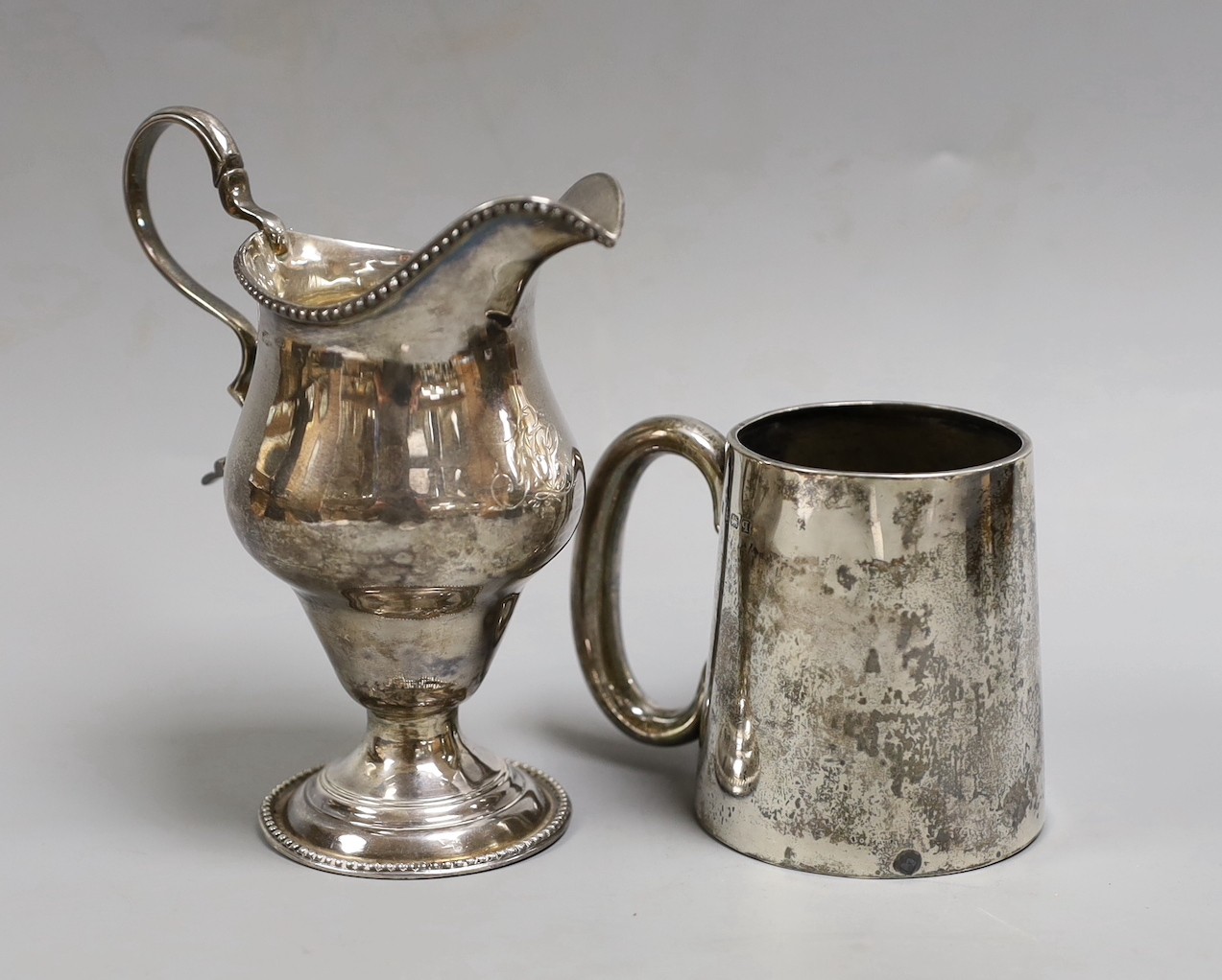A George III silver inverted pear shaped cream jug, marks rubbed, 72mm and a later silver christening mug.                                                                                                                  