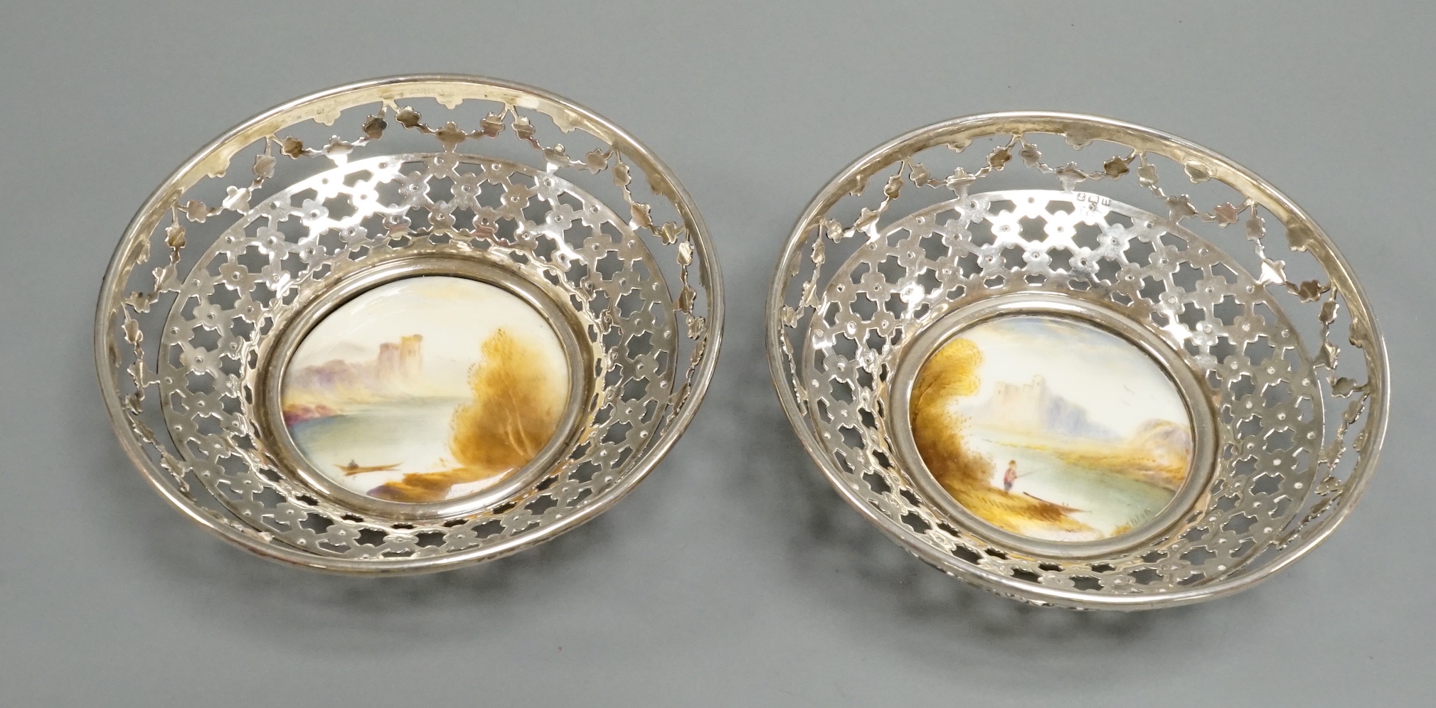 A pair of George V pierced silver mounted Royal Worcester panel bon bon dishes, painted by Raymond Rushton, hallmarked for Sanders & MacKenzie, Birmingham, 1912, diameter 10.5cm.                                          