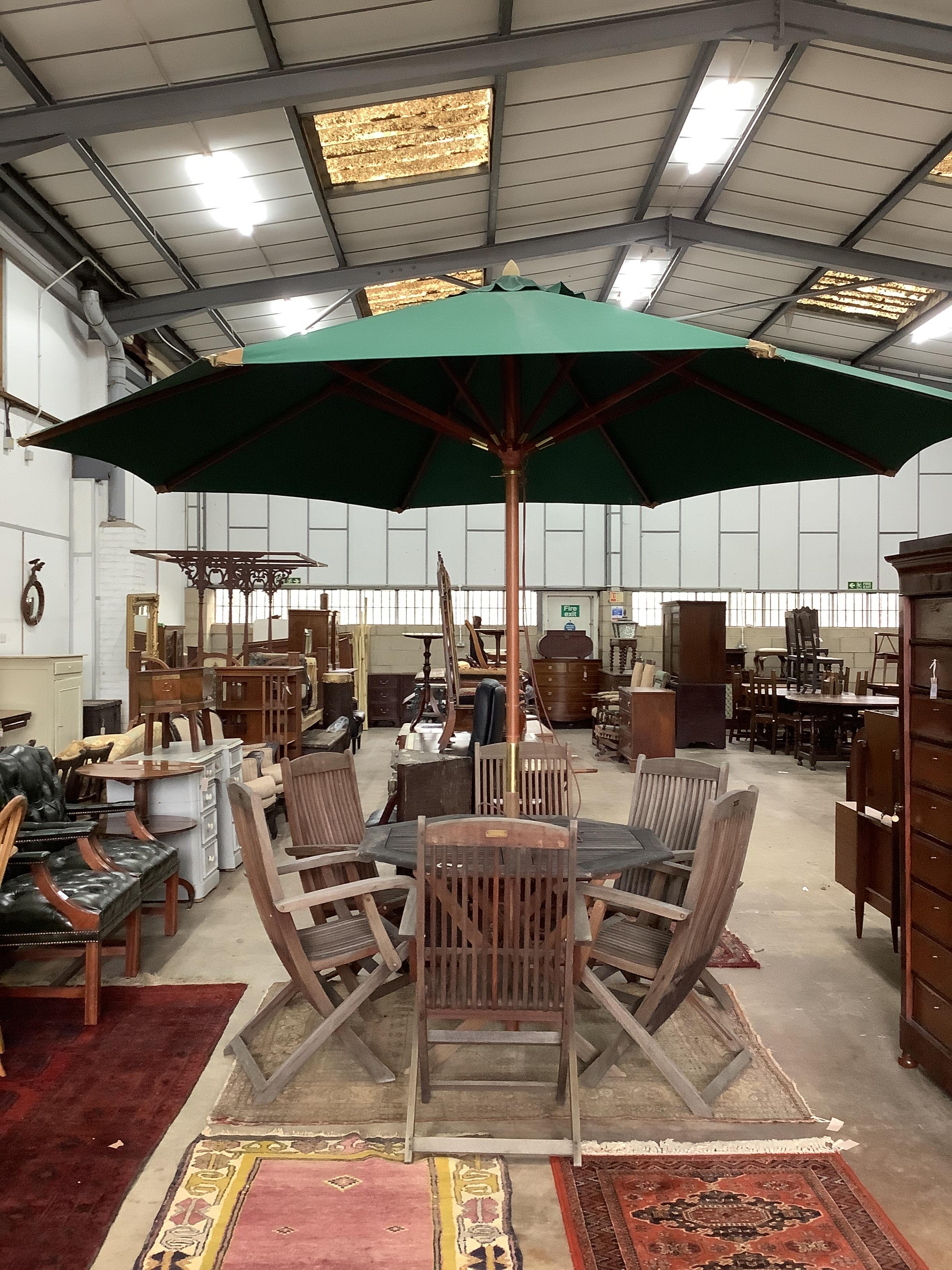 A weathered teak octagonal garden table, width 112cm, height 72cm together with six Beaufort weathered teak folding garden elbow chairs and green canvas crank parasol                                                      