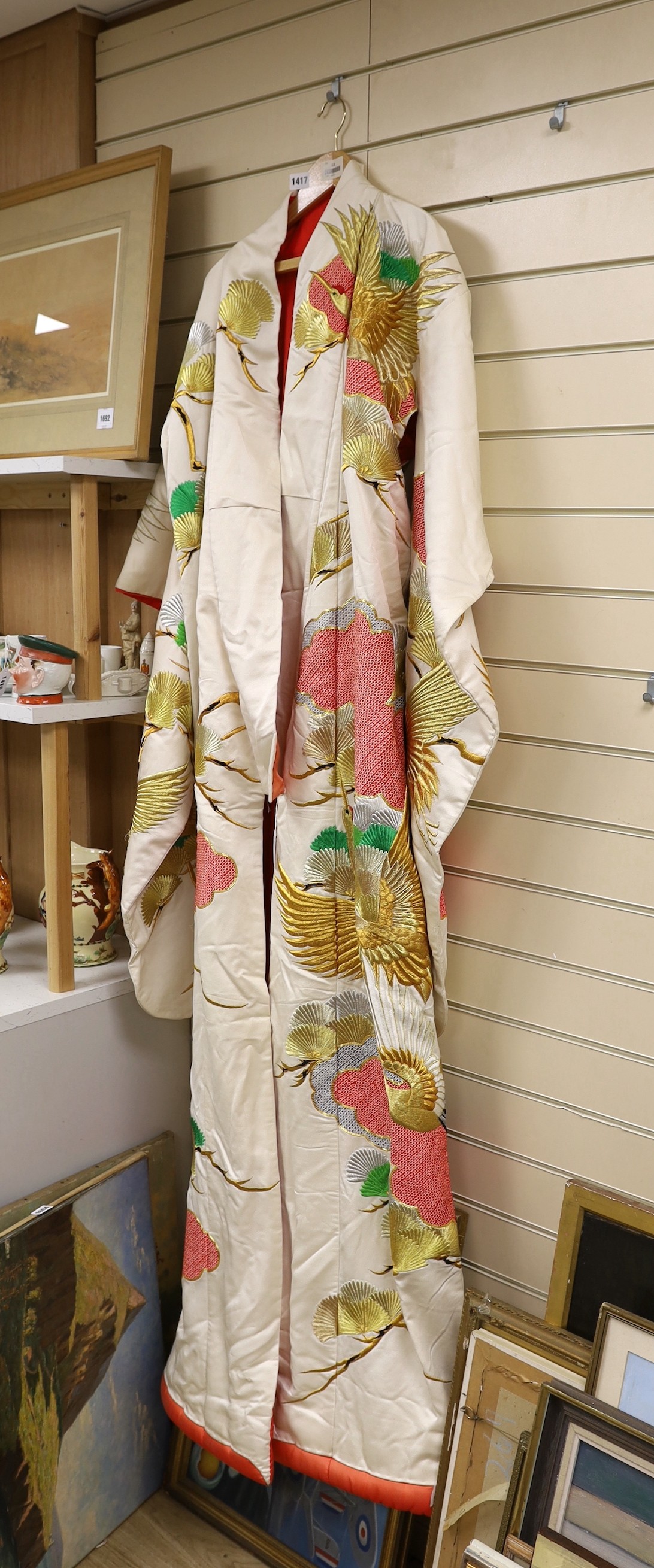 A Japanese cream ground ceremonial kimono, embroidered with coloured silks and metallic embroidery, in an all over design, with flame red silk lining                                                                       