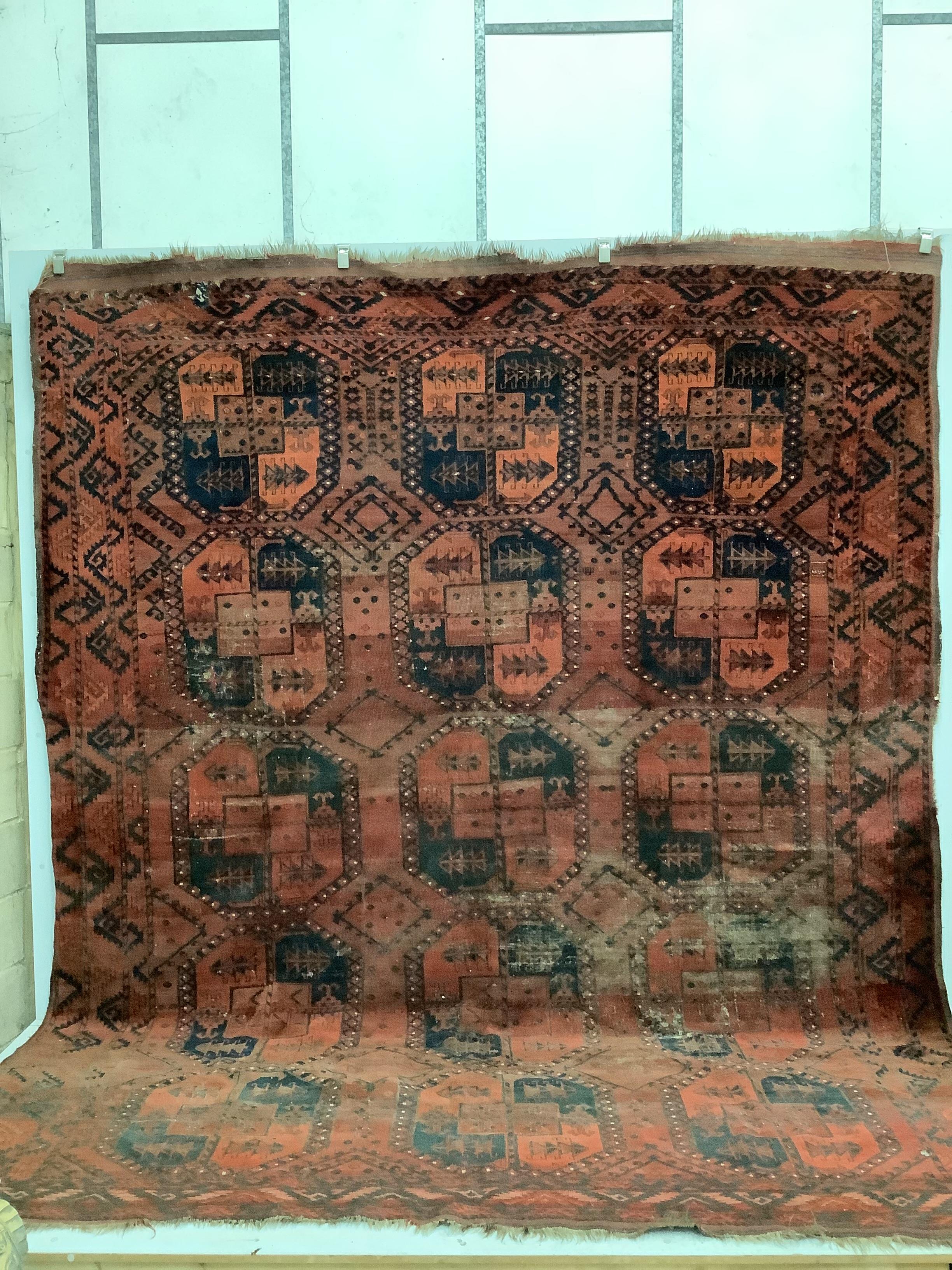 An antique Afghan red ground carpet, 340 x 278cm, worn and holed                                                                                                                                                            