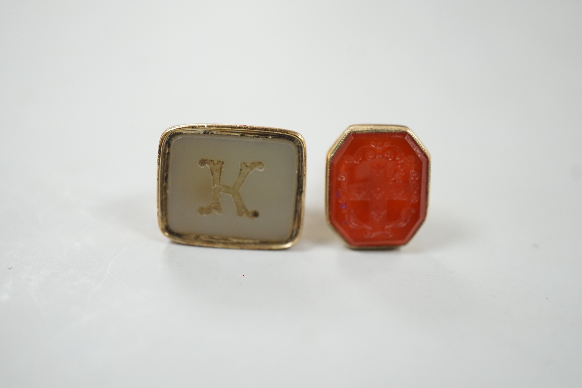 A 19th century yellow metal overlaid and white carnelian set fob seal, the matrix carved with the letter K, 27mm and a 1970's 9ct gold and carnelian set fob seal, the matrix carved with an armorial.                      