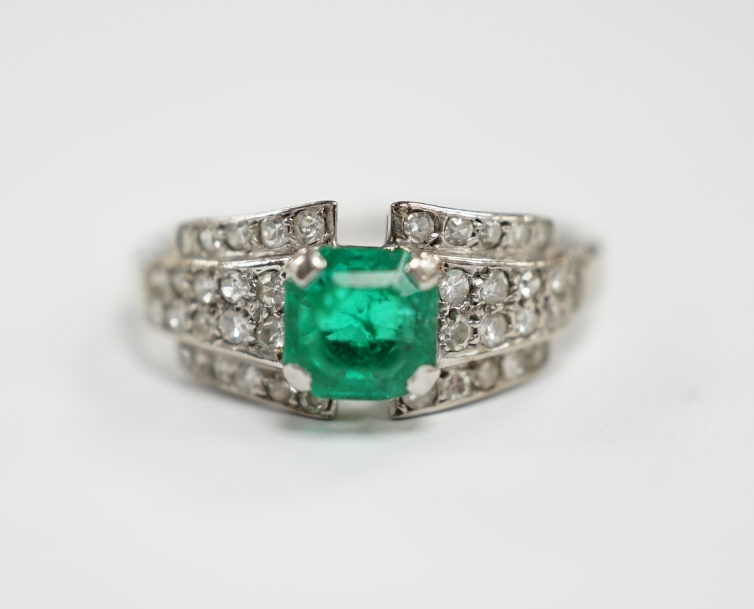 A white metal and octagonal cut emerald set dress ring, with diamond cluster set shoulders, size O, gross weight 3.6 grams.                                                                                                 