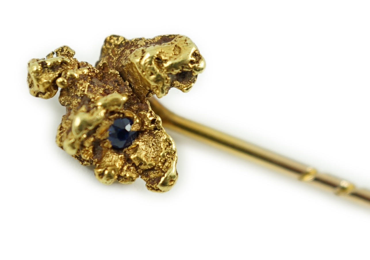 A late Victorian yellow metal and single stone sapphire set 'nugget' stick pin, 62mm, gross weight 3.2 grams.                                                                                                               