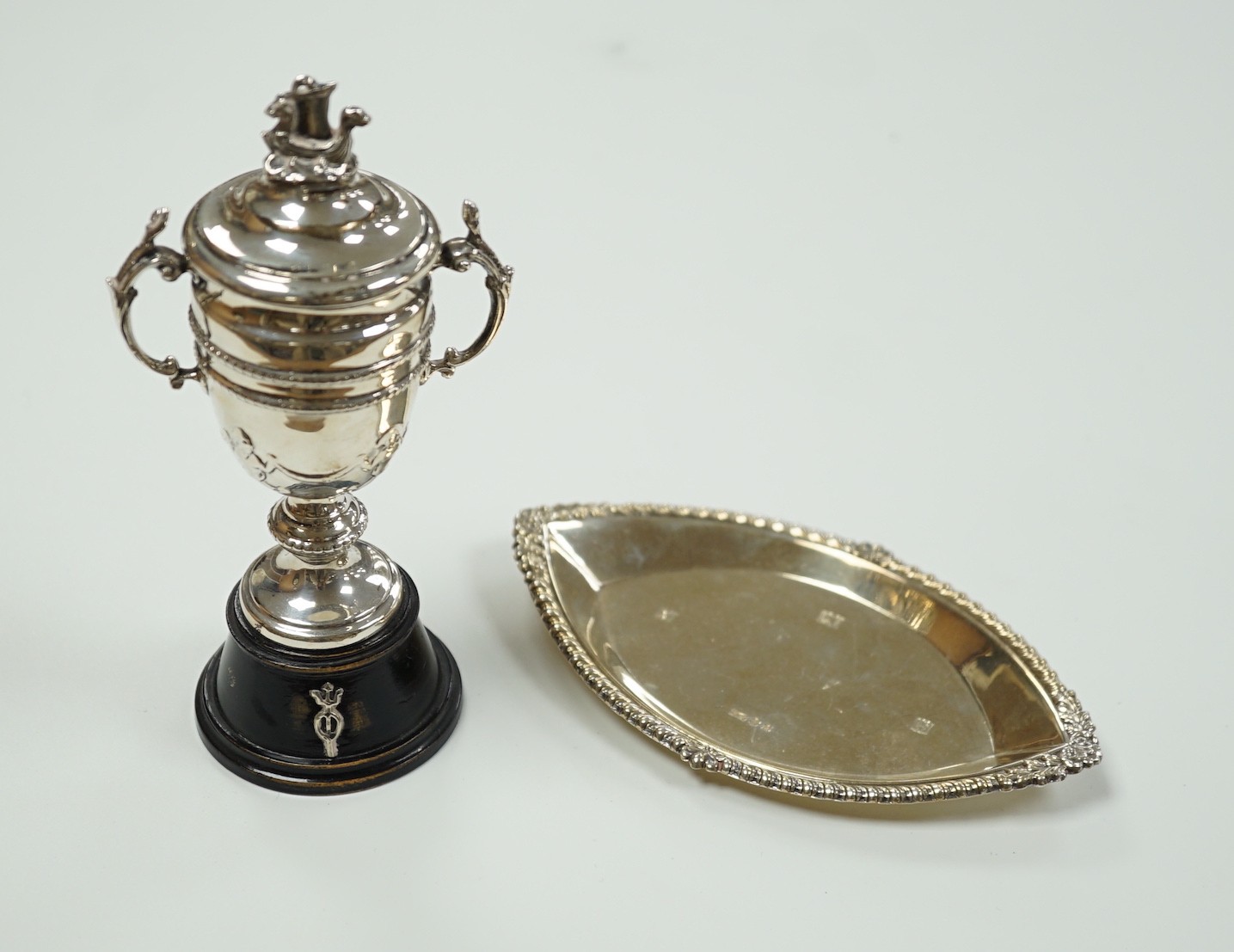 A miniature George V Scottish silver lidded trophy cup, on stand, Edinburgh, 1913, overall 14cm and a George V silver navette shaped dish.                                                                                  