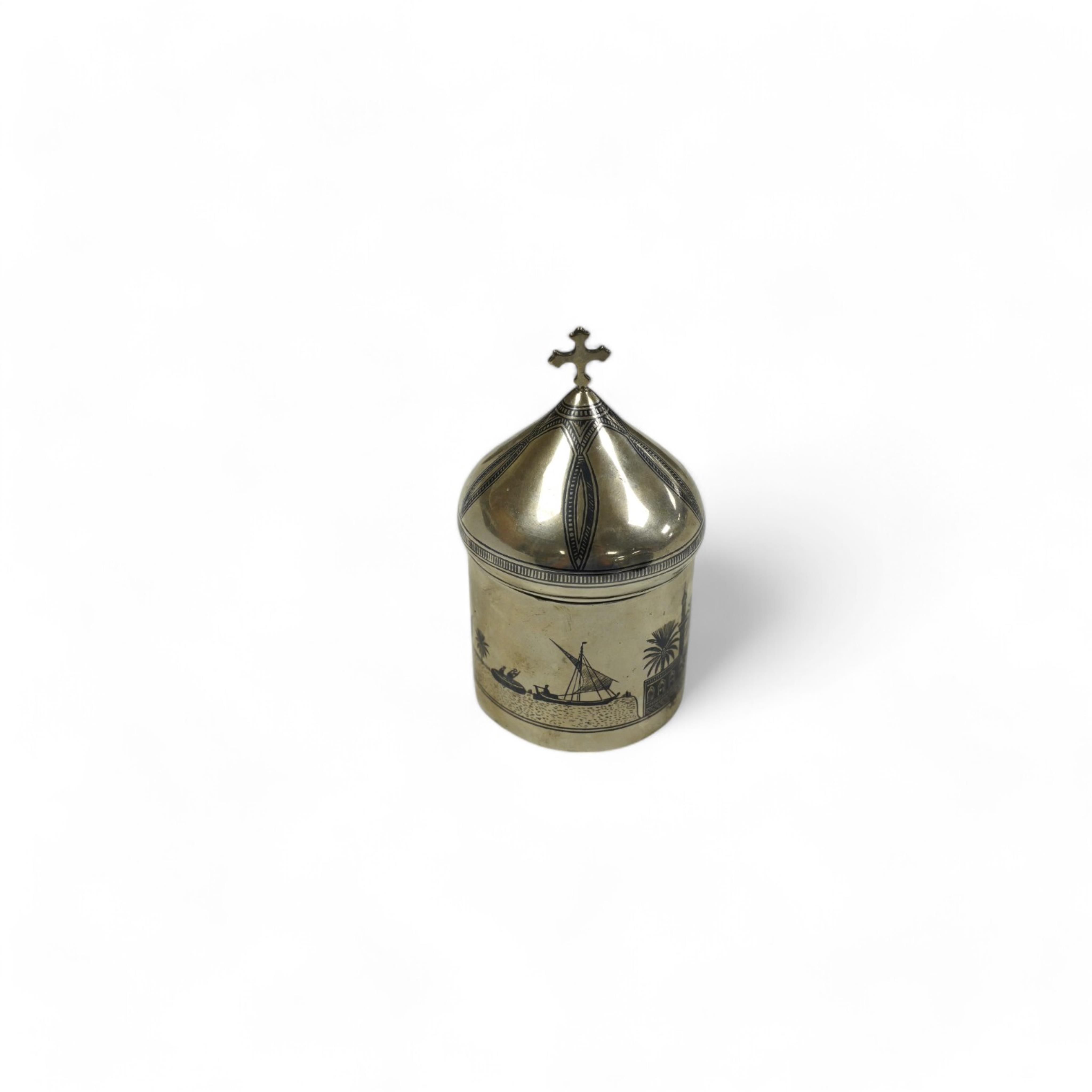 A Middle Eastern white metal and niello box and cover, with cross finial, 11.8cm, gross weight 4.4oz. Condition - poor to fair                                                                                              