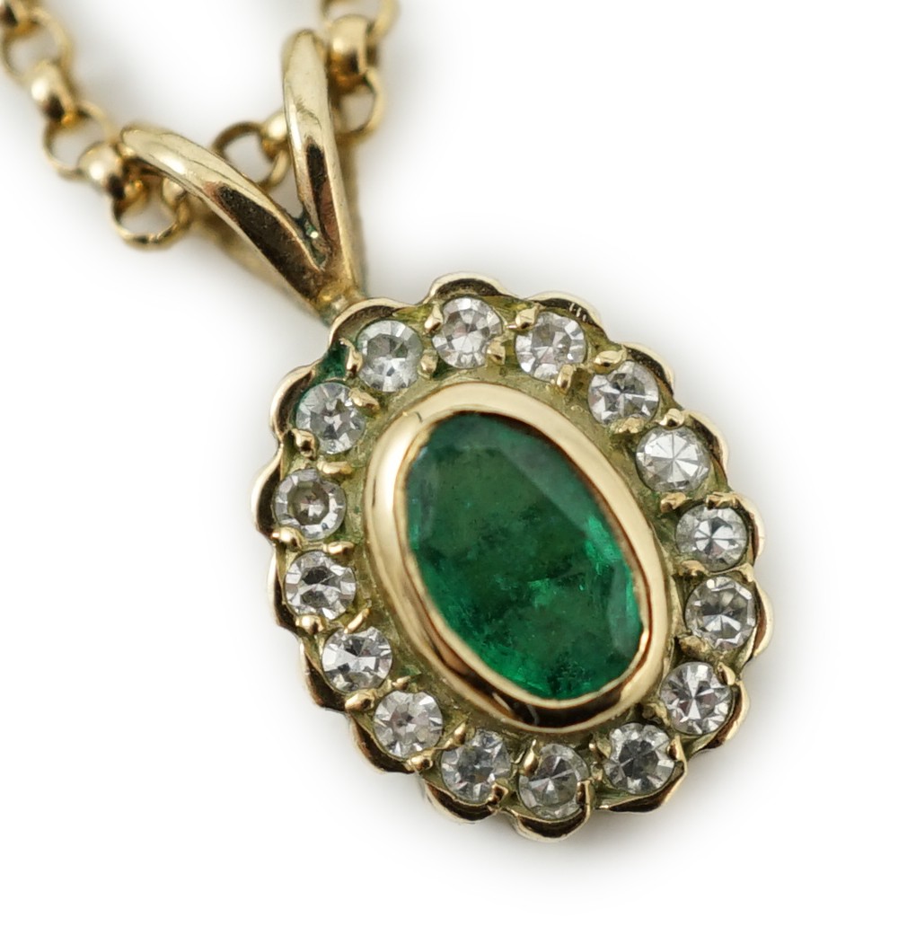 A modern 9ct gold, emerald and diamond set oval cluster pendant, 16mm, on a 9ct gold chain, 44cm, gross weight 4.1 grams.                                                                                                   