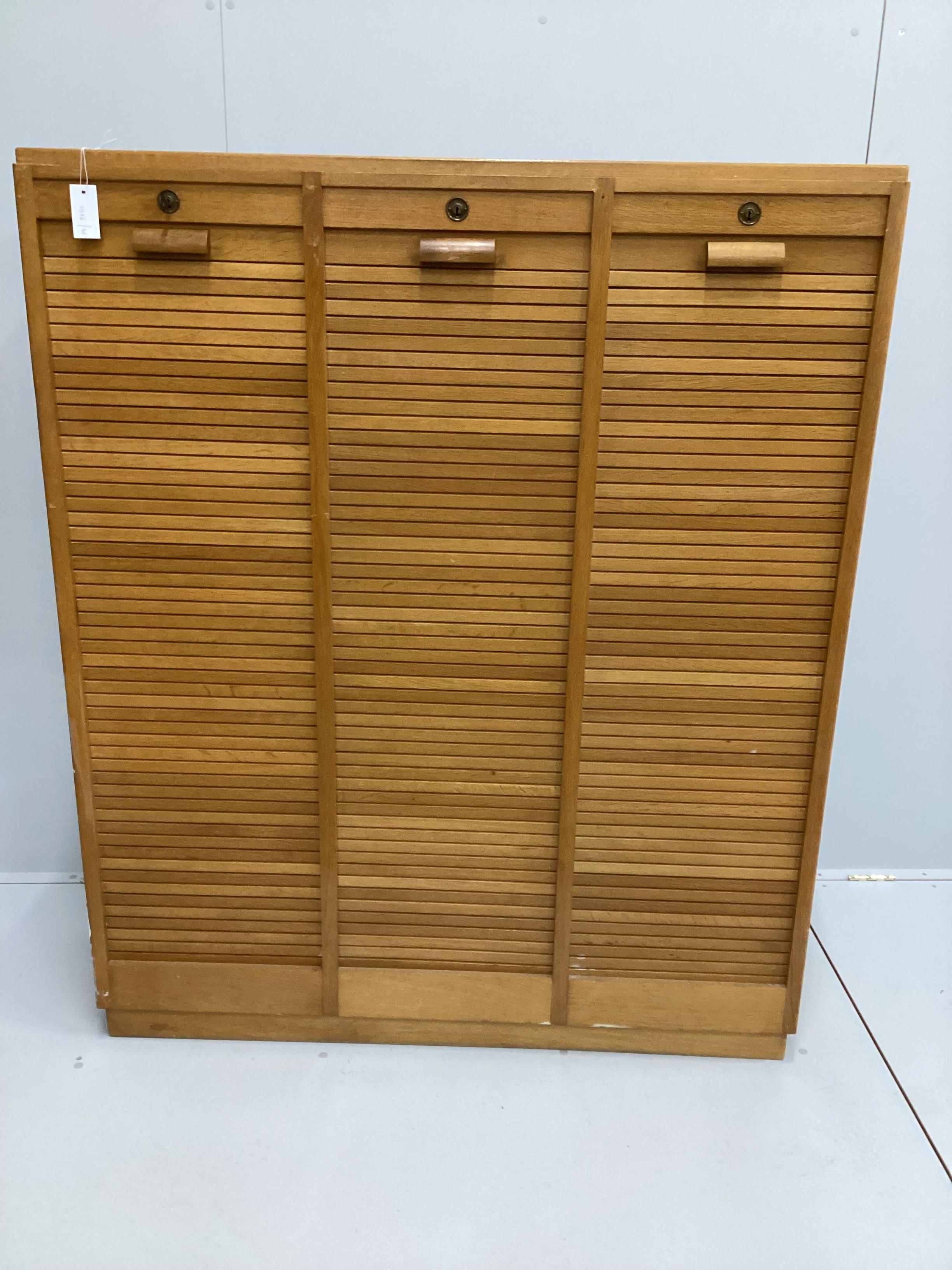 A mid century oak triple tambour filing cabinet, width 124cm, depth 36cm, height 151cm                                                                                                                                      