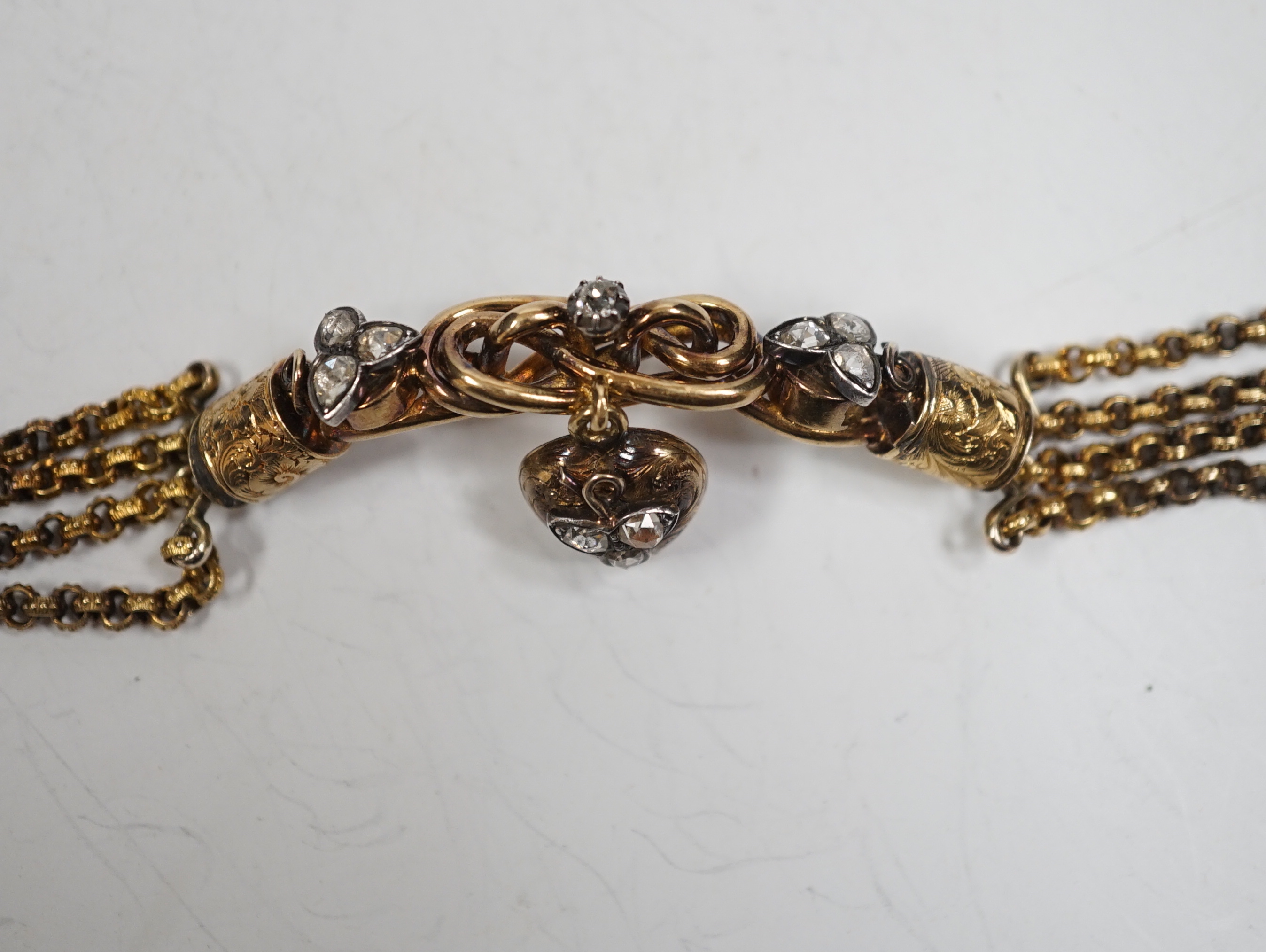 An antique yellow metal (test as 18ct) and rose cut diamond set triple strand bracelet, the central scrolling motif, hung with diamond set heart shaped charm, approx. 17cm, gross weight 30 grams.                         