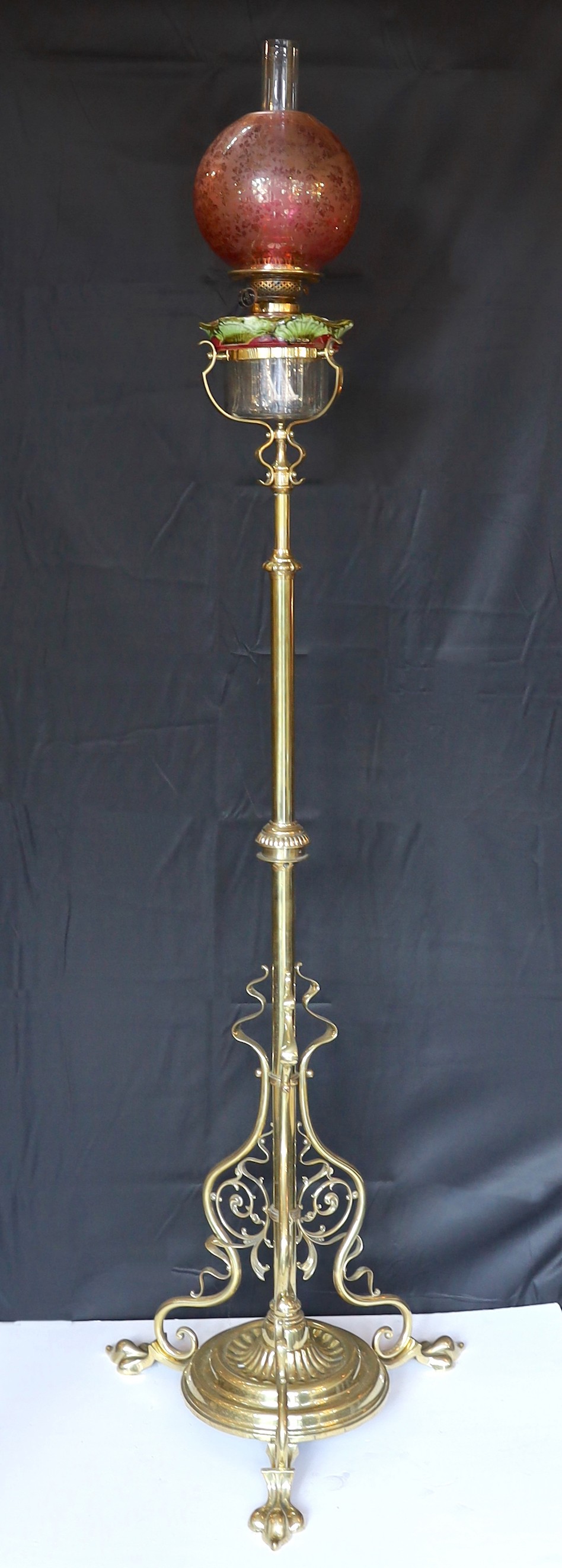 An Edwardian brass telescopic oil lamp standard, with later edged cranberry glass shade and duplex mechanism, height 168cm. width 52cm                                                                                      