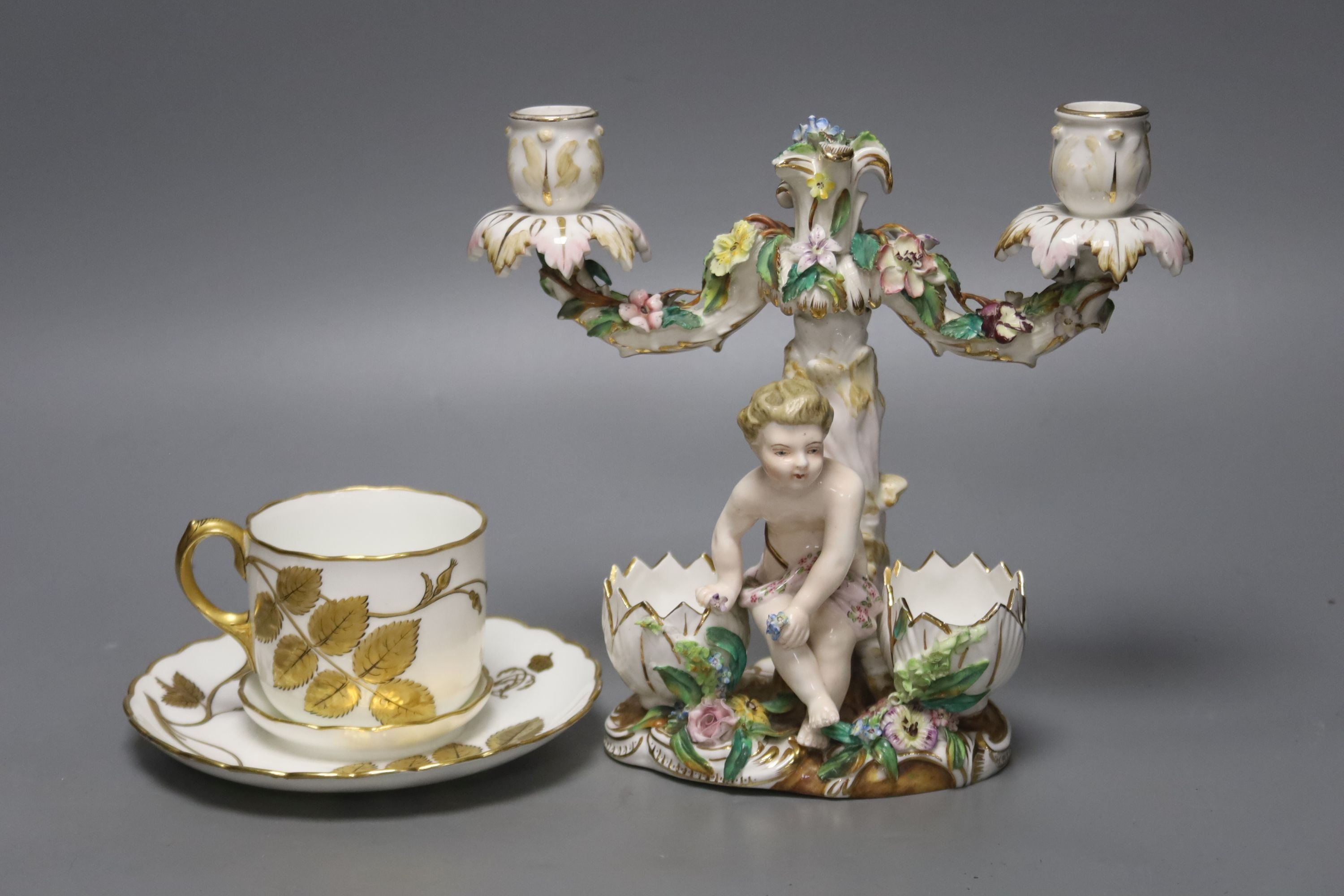 A John Bevington figural candelabra, height 19cm, and a cup and trembleuse saucer                                                                                                                                           