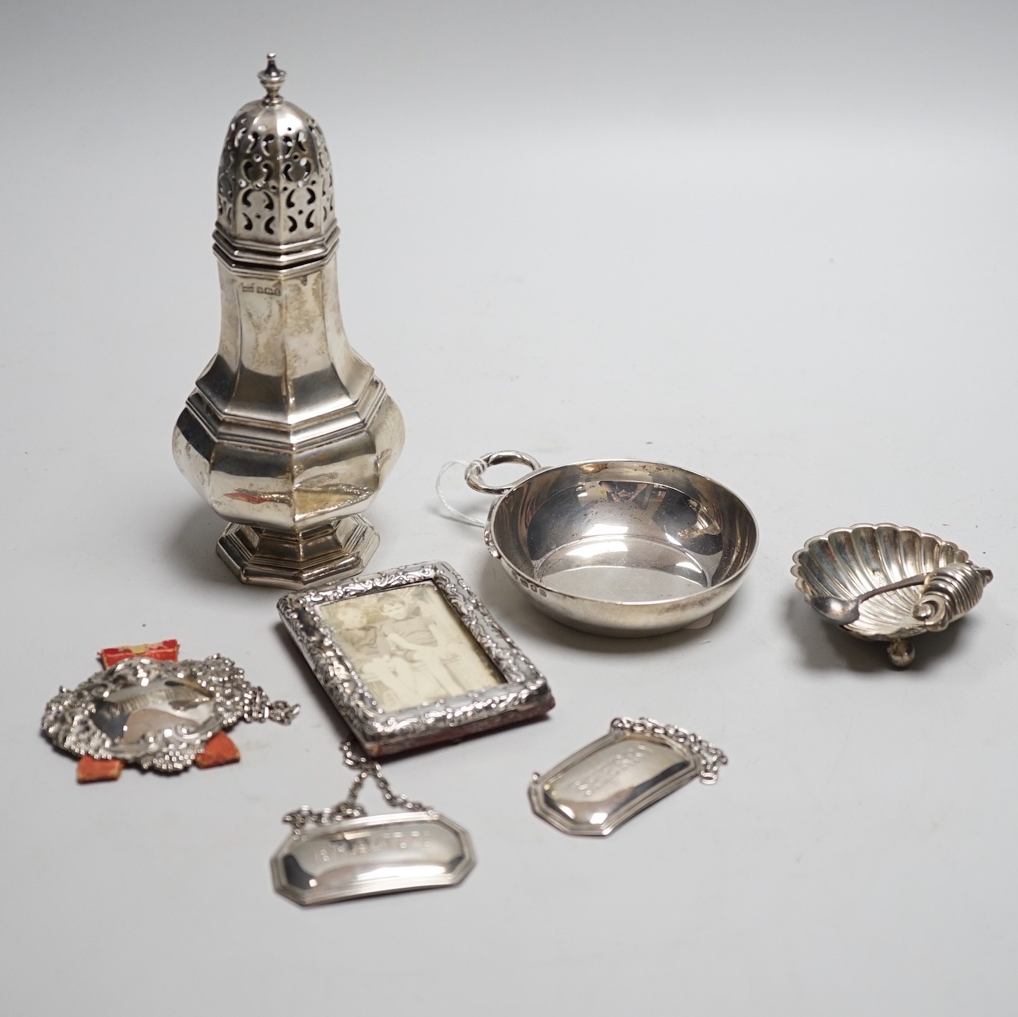 A George V silver octagonal baluster sugar caster, by Walker & Hall, 16.4cm, a modern silver taste du vin, three modern silver wine labels, a silver shell salt, silver condiment spoon and a late Victorian miniature silve