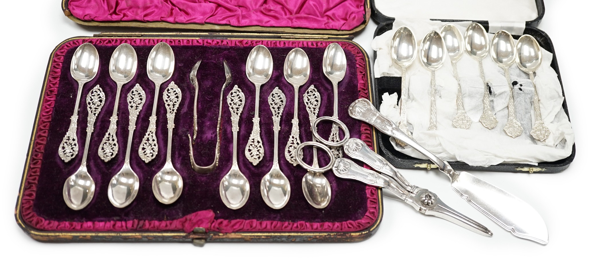 A cased set of twelve Victorian silver teaspoons, with pierced terminals by William Comyns, London 1889, with a damaged pair of matching sugar tongs, a cased set of six later teaspoons, a pair of George IV silver King's 