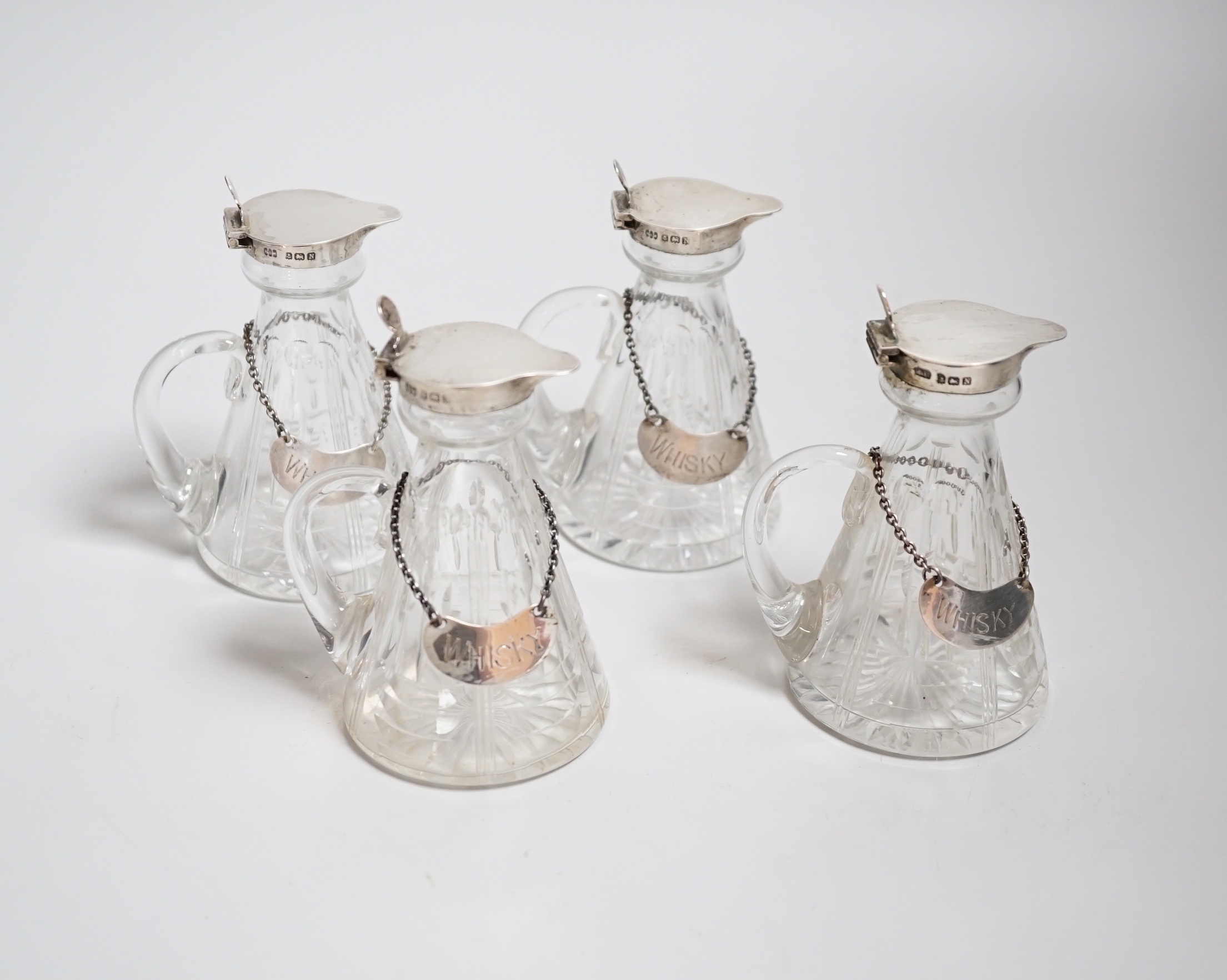 A set of four George VI silver mounted cut glass whisky noggins by Hukin & Heath, Birmingham, 1937, 11cm and four silver whisky labels, same date and maker.                                                                