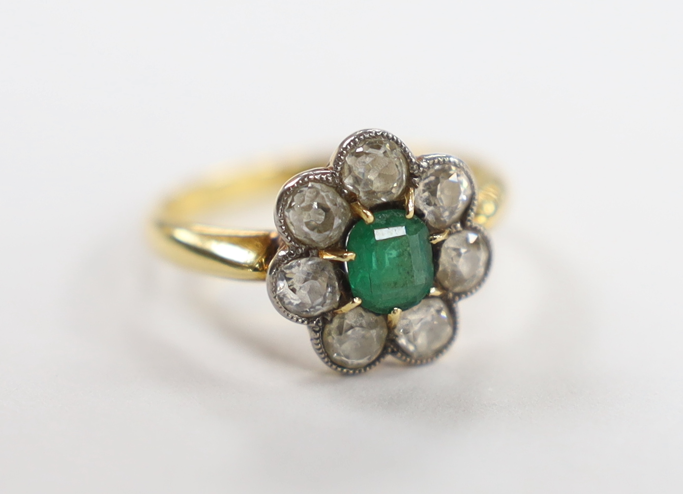 An 18ct, emerald and diamond set circular cluster ring, size L, gross weight 3.3 grams.                                                                                                                                     