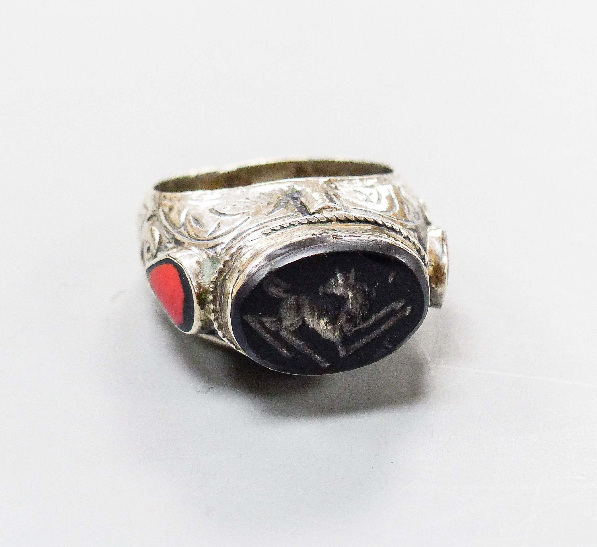 A continental engraved white metal and oval intaglio black onyx ring, with two colour enamel set shoulders, size S/T, gross weight 18.8 grams.                                                                              