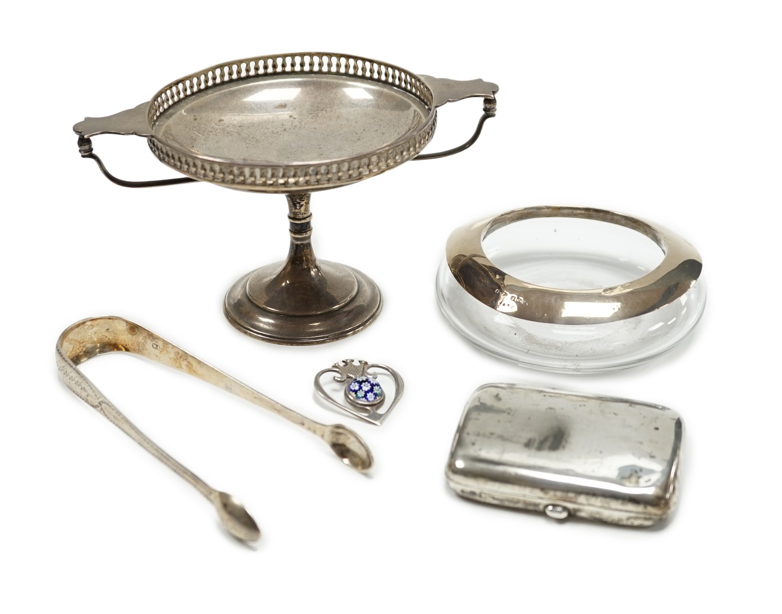 A George V silver tazza, a silver cigarette case, a pair of George III silver sugar tongs, a silver mounted glass shallow dish and a modern silver and lass inset pendant.                                                  