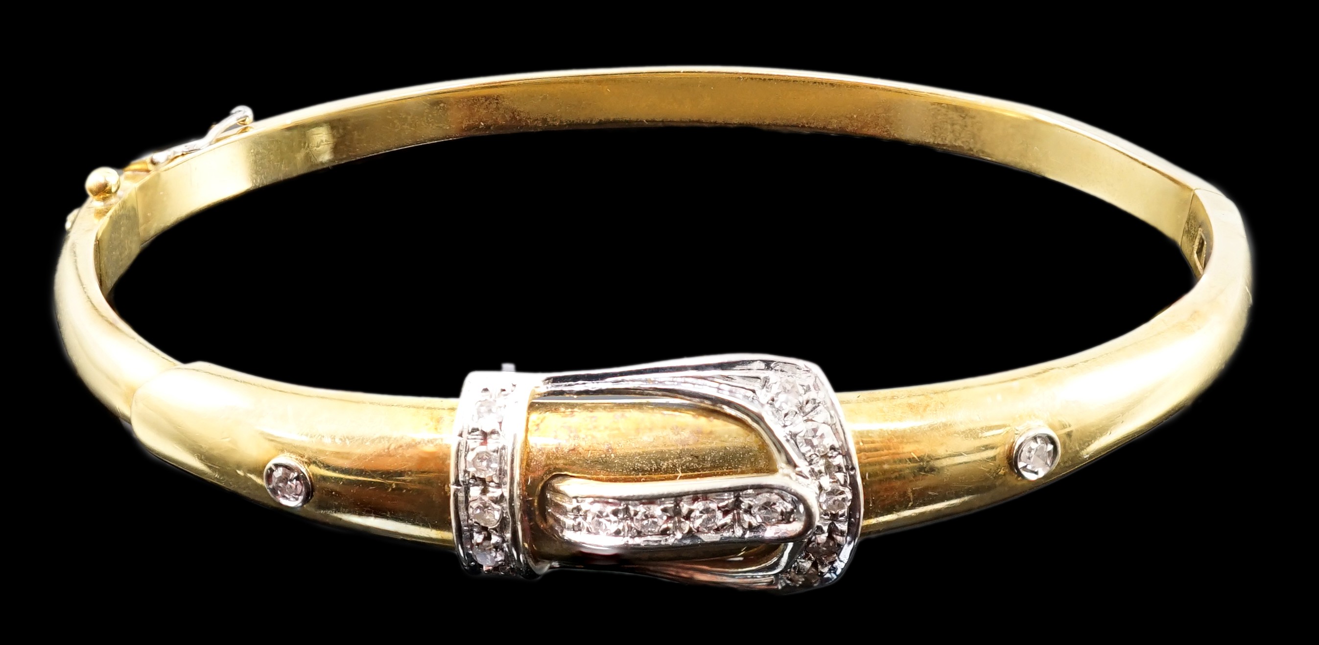 A gold and diamond set hinged bangle with central buckle motif                                                                                                                                                              