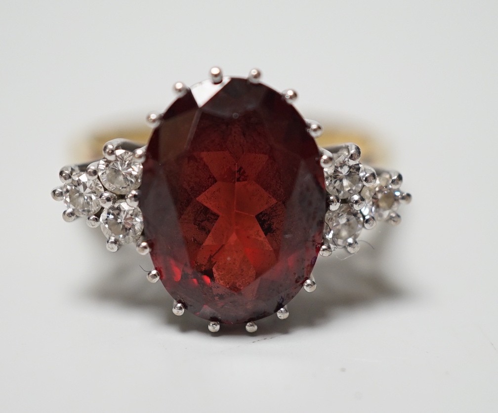 A modern 18ct gold and oval cut garnet set dress ring, with six stone diamond set shoulders, size M/N, gross weight 4.8 grams.                                                                                              