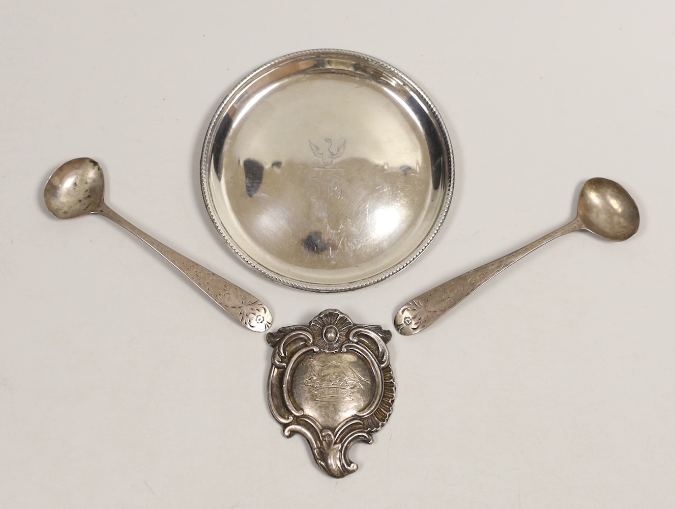 A George III silver glass coaster, William Plummer, London, 1781, 91mm, together with a pair of early 19th century Irish silver condiment spoons and a white metal cartouche.                                               