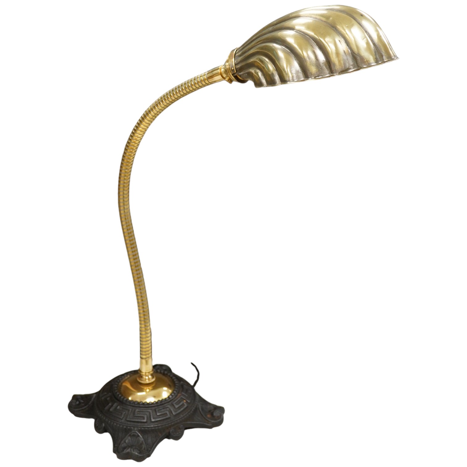 An English desk lamp wrought iron base with flexy brass arm and brass shell shape shade, early 20th century, wired, 55cm high, base 17cm diameter. Condition - good                                                         