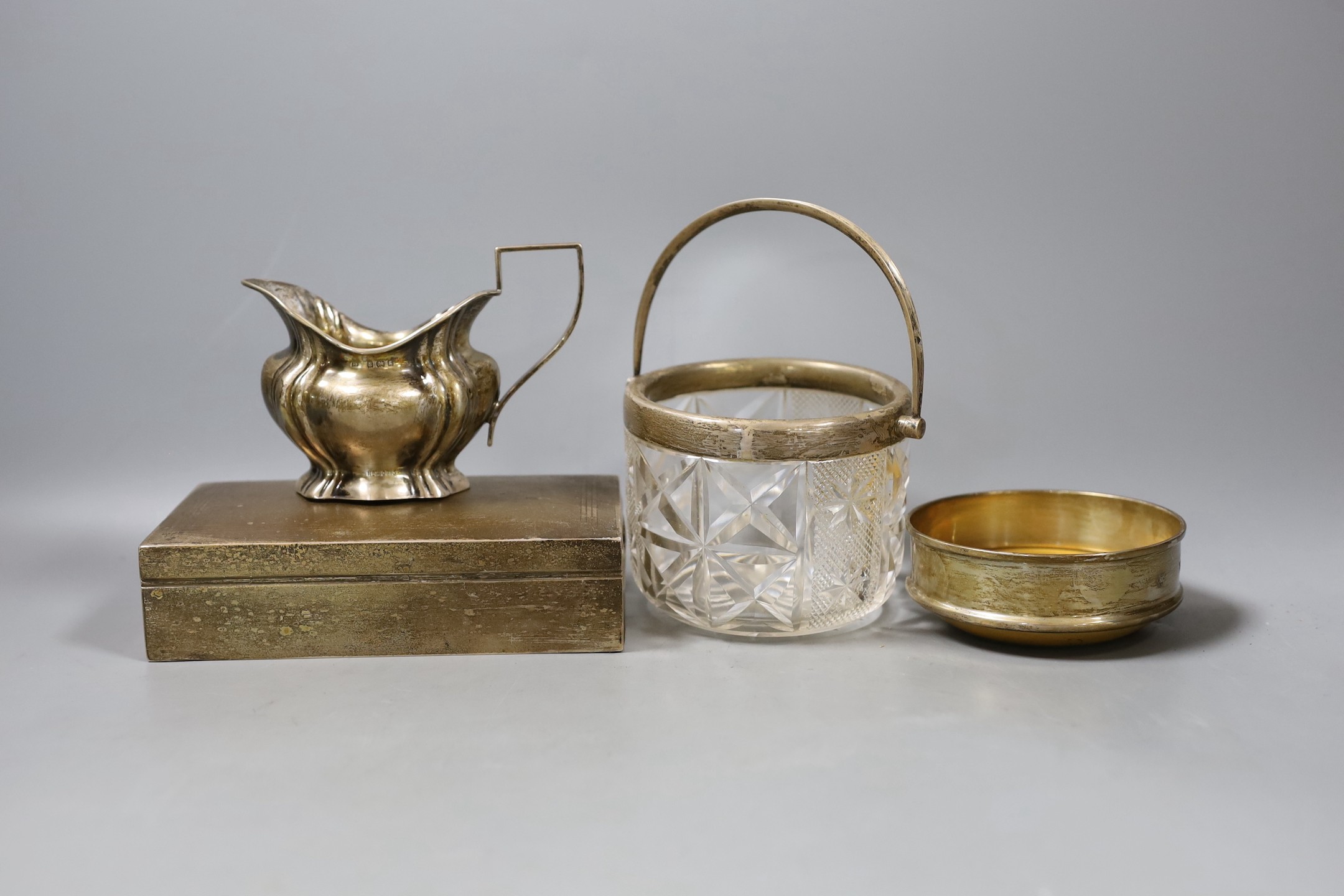 A silver cigarette box, 16.7cm, a silver cream jug, a silver mounted glass jar and a modern silver mounted coaster.                                                                                                         