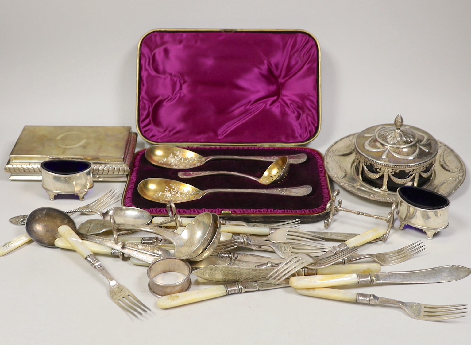 A late 19th century Hanau white metal butter dish stand, with blue glass liner, diameter 18.3cm, a sterling mounted cigarette box, a cased Victorian three piece silver cutlery dessert set, a pair of Victorian silver fidd