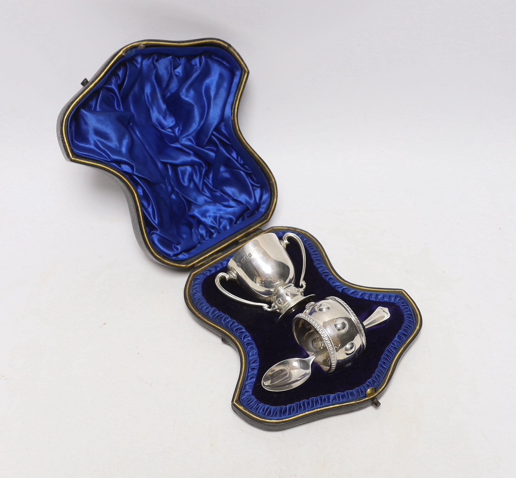 A cased Edwardian matched silver christening pair, (egg cup and napkin ring), Wakeley & Wheeler, London, 1905/6, with associated silver spoon.                                                                              