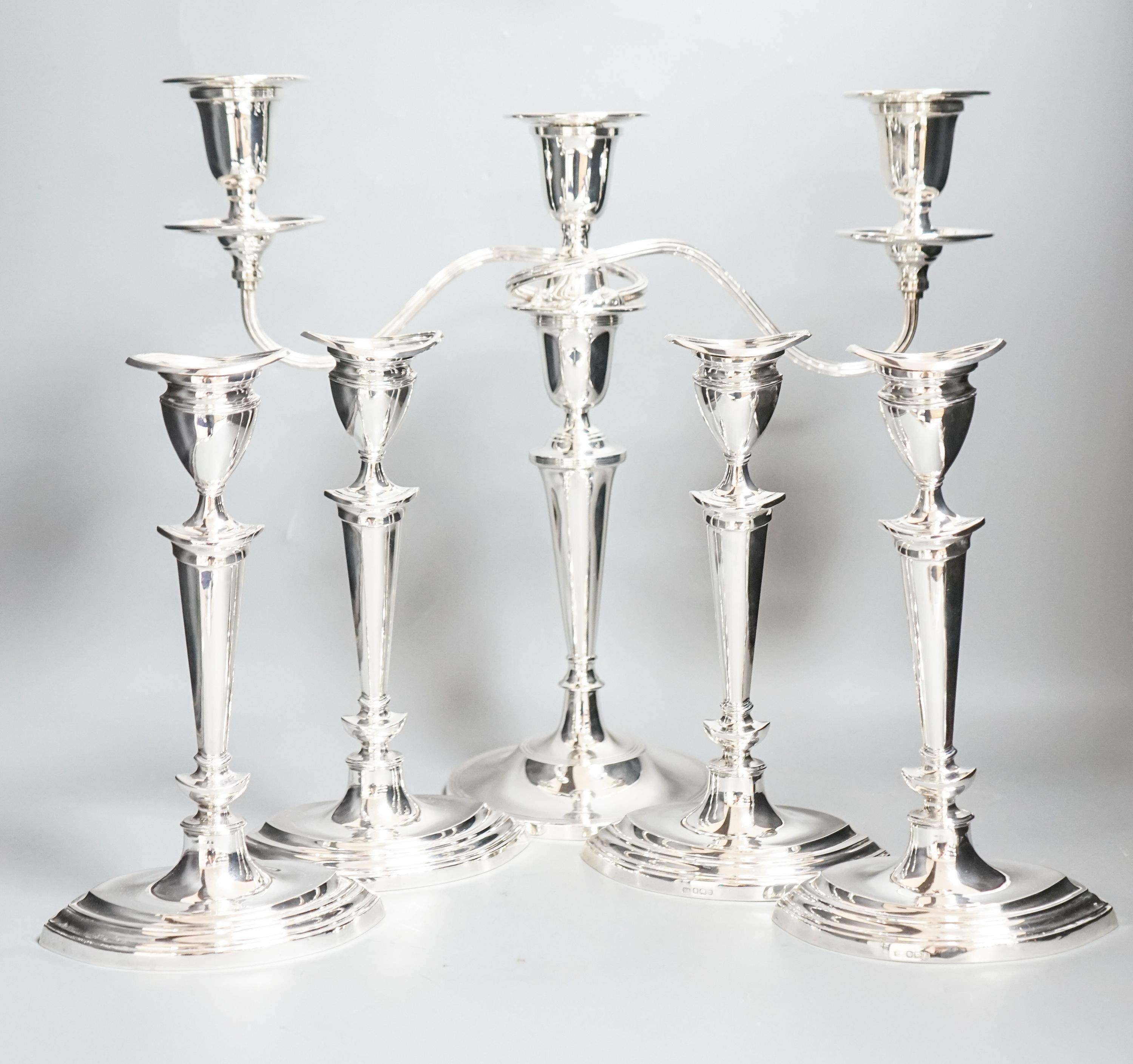 A set of four George V silver oval candlesticks, Atkin Brothers, Sheffield, 1911, height 24.2cm, together with a later silver two branch, three light candelabrum, height 35cm, all weighted.                               