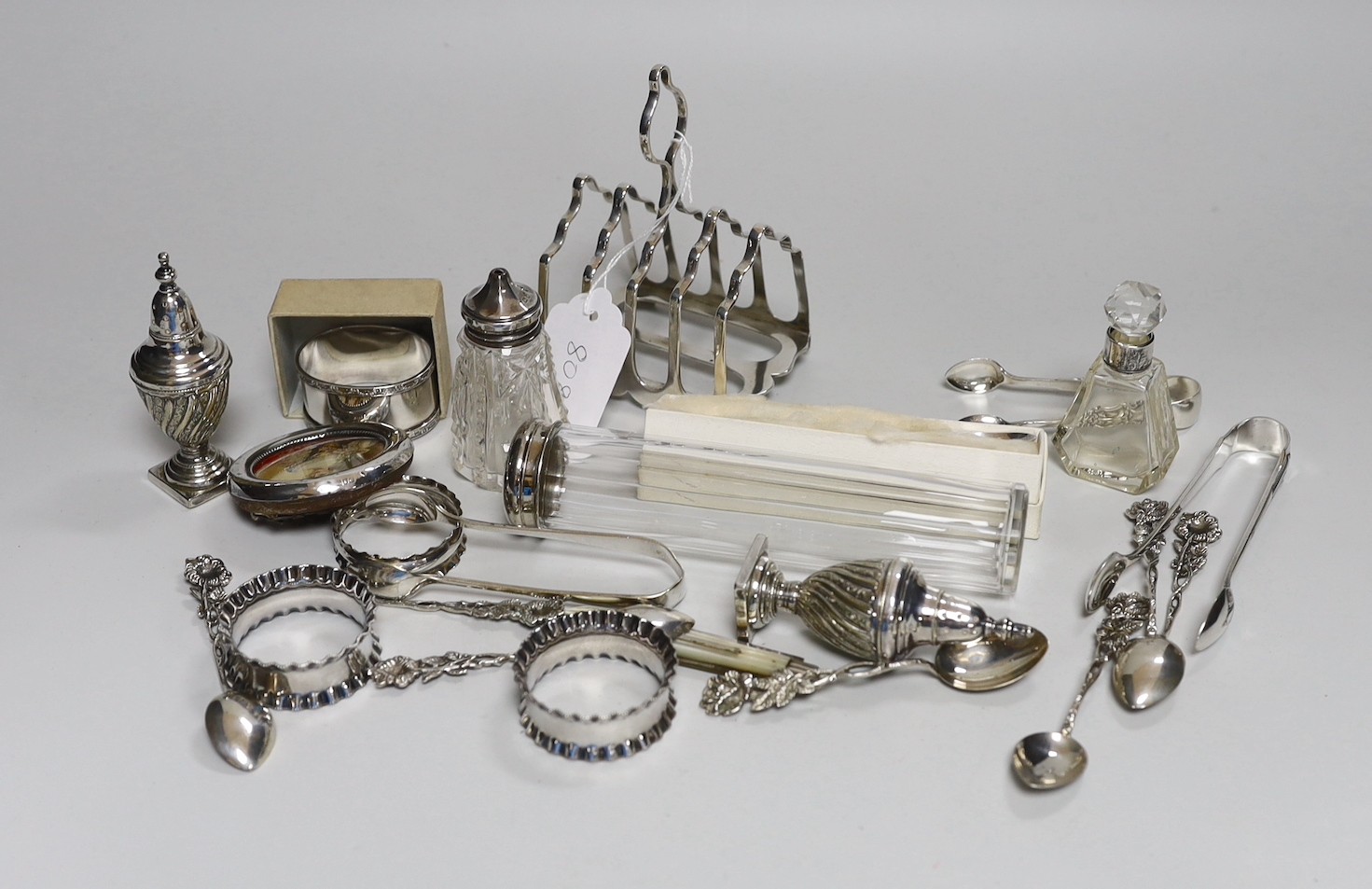 Assorted minor silver ware including a George V toast rack by James Dixon & Sons, 86mm, two napkin rings, a mounted glass toilet jar and condiment, pair of sugar tongs, a fruit knife, a commemorative spoon, a mounted sma