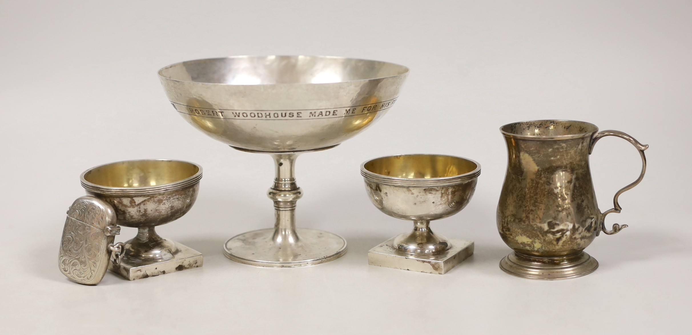 An Edwardian planished silver tazza, with engraved inscription, Robert Woodhouse, London, 1905, diameter 14cm, a small George III silver mug (a.f.), London, 1795, a pair of George V silver pedestal salts and a silver ves