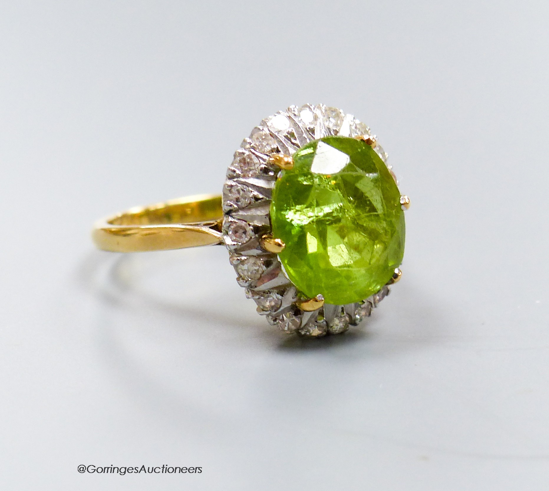 An 18ct, peridot and diamond oval cluster set dress ring, size T, gross 7 grams.                                                                                                                                            