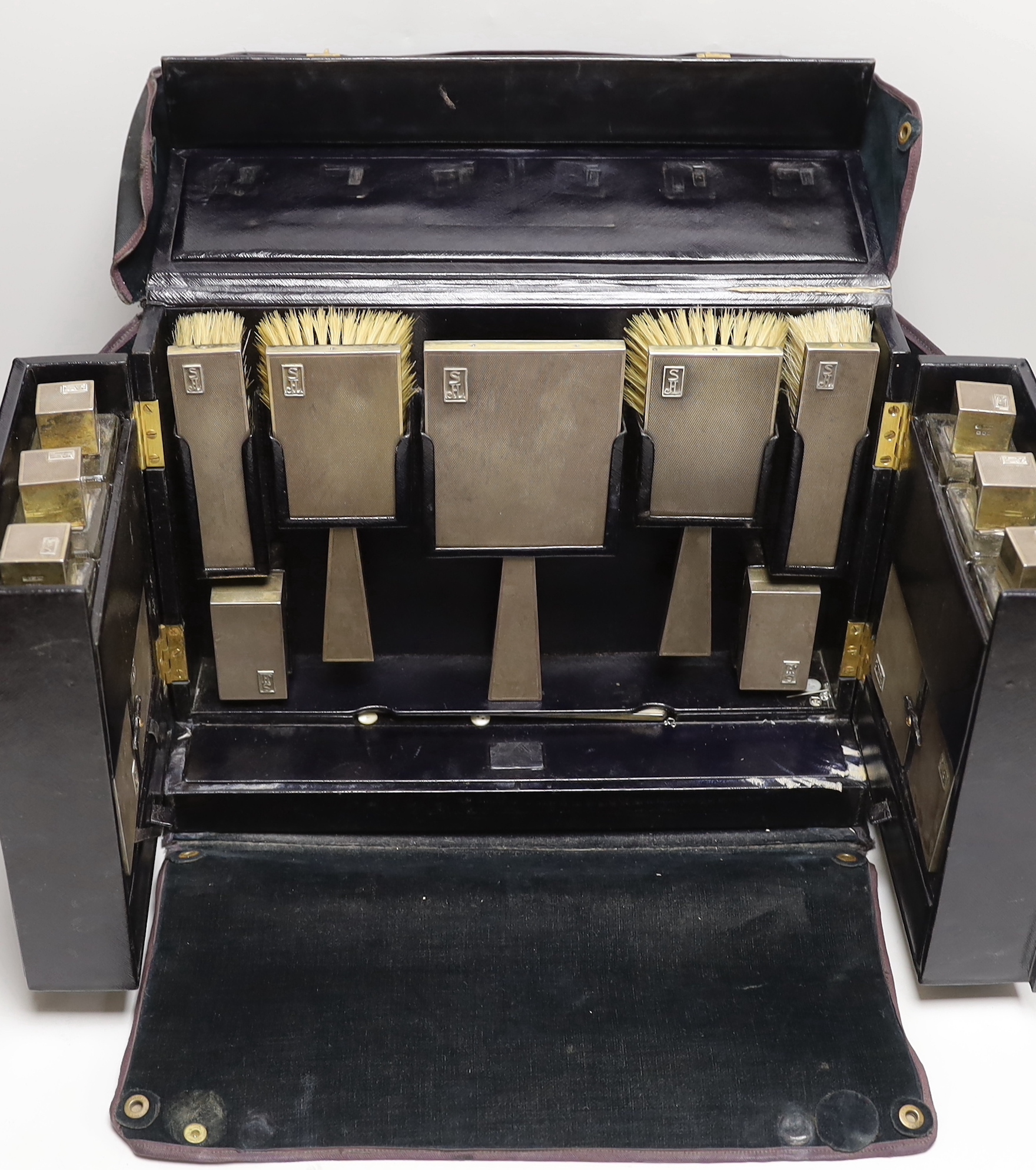 A George VI leather travelling vanity case, containing seventeen monogrammed silver mounted items, including ten mounted glass toilet jars, two boxes, four brushes and a hand mirror, Asprey & Co, London, 1936, case width