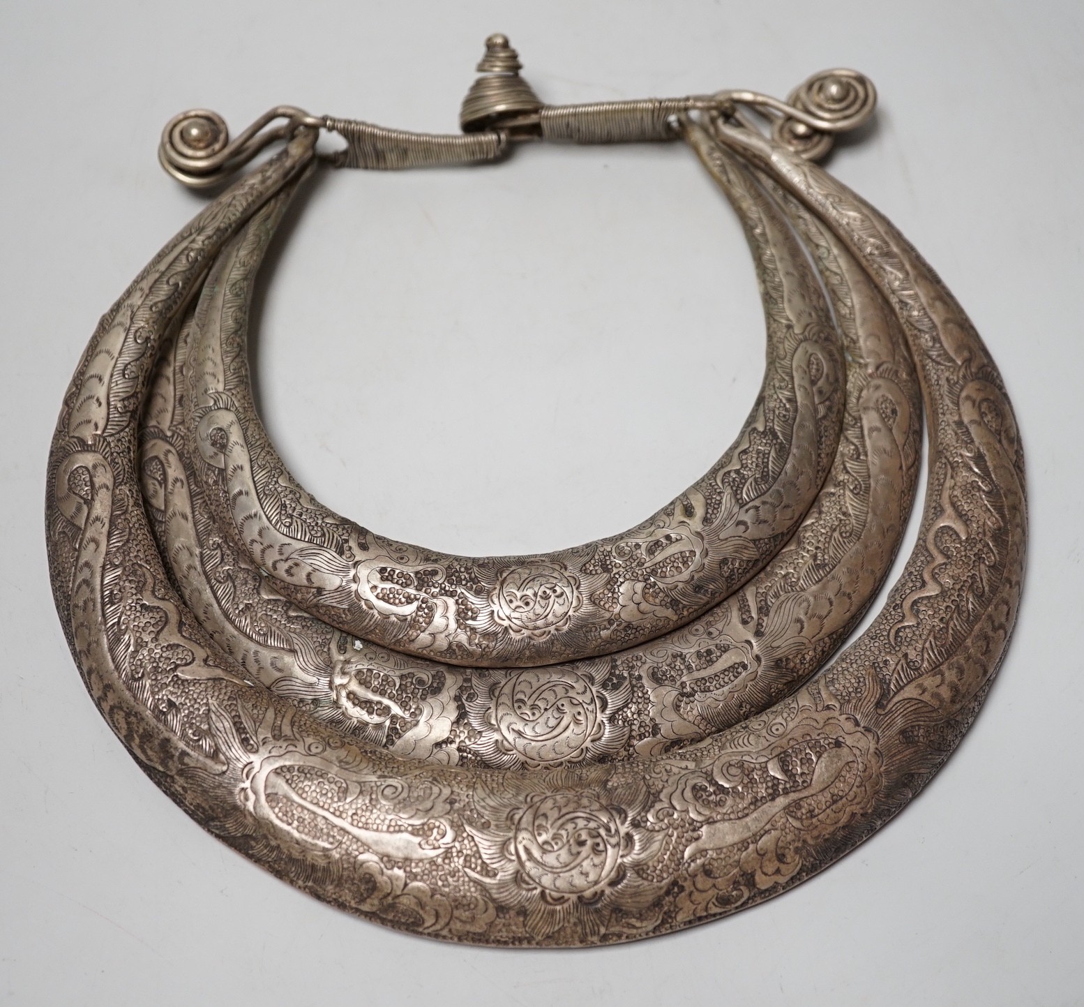 A Chinese Miao white metal triple necklace, repousse worked with dragons and twin fish, 25cm wide                                                                                                                           