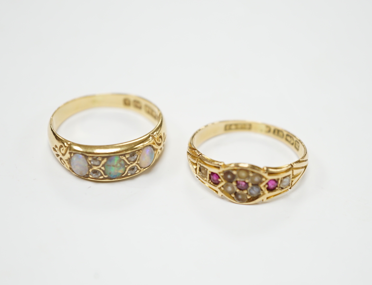 A late Victorian 18ct gold and three stone white opal set half hoop ring, with diamond chip spacers, size M (opal chipped), together with a similar 18ct gold, ruby and seed pearl ring, size K/L, gross weight 5.7 grams.  