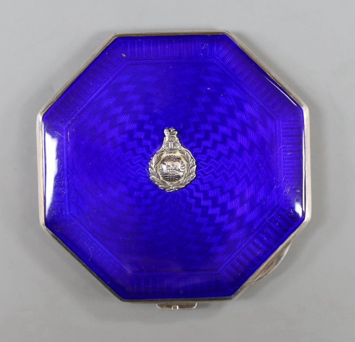 A George VI octagonal silver and blue enamel compact, with regimental appliqué, Birmingham, 1937, 80mm.                                                                                                                     