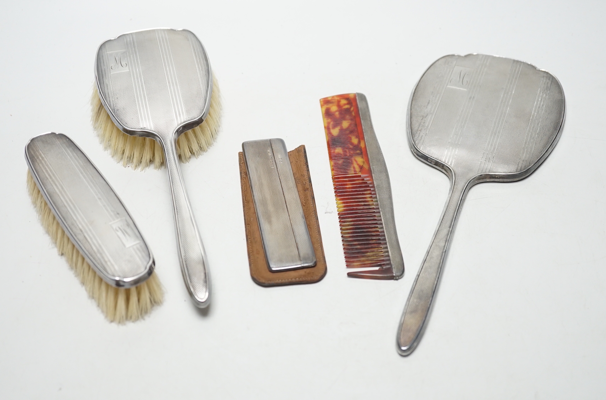 A George V silver backed four piece dressing table set, Birmingham, 1934 and one other silver cased comb.                                                                                                                   