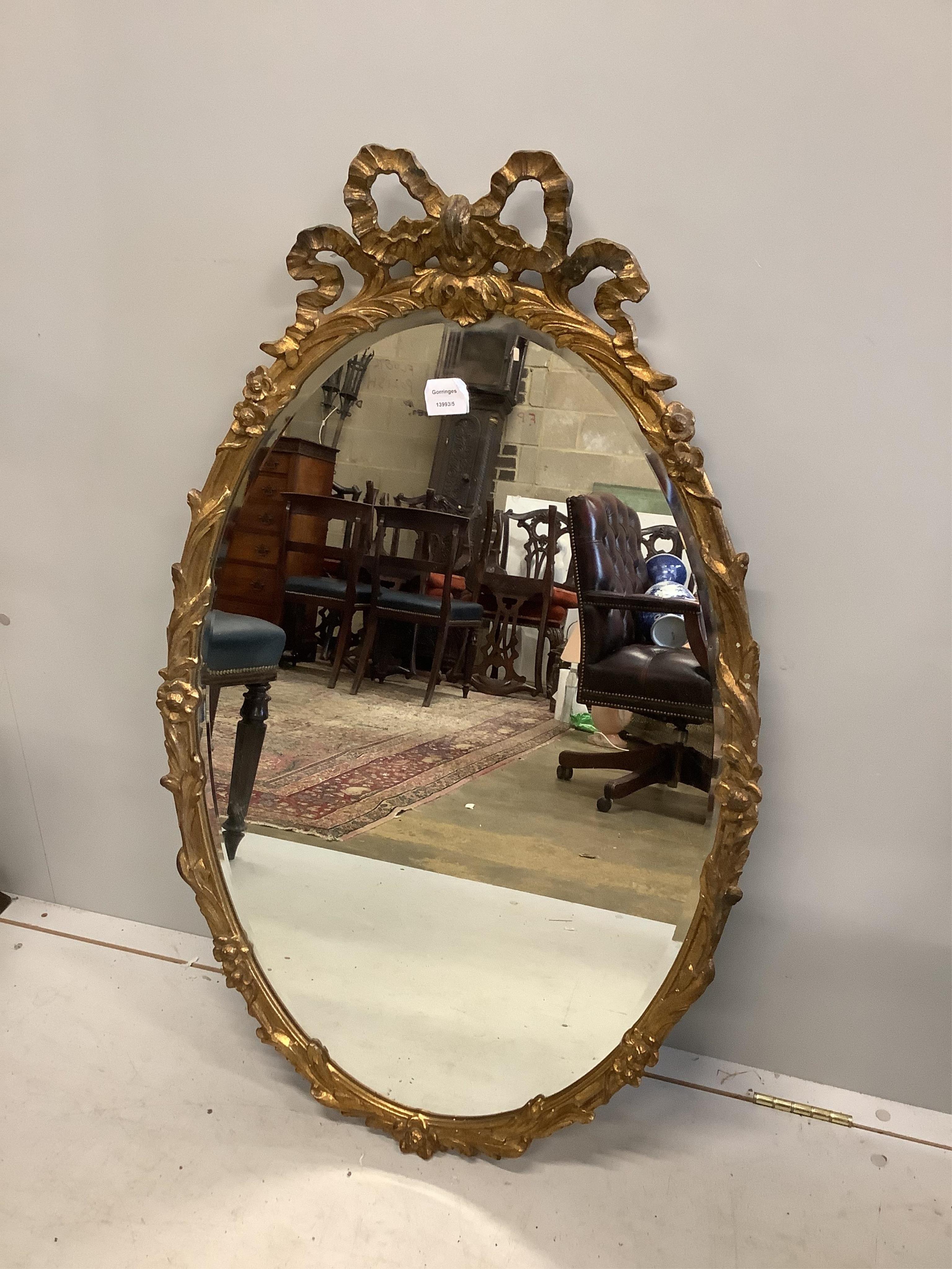 A George III style carved giltwood composition oval wall mirror with ribbon crest, width 62cm, height 102cm. Condition - fair to good                                                                                       