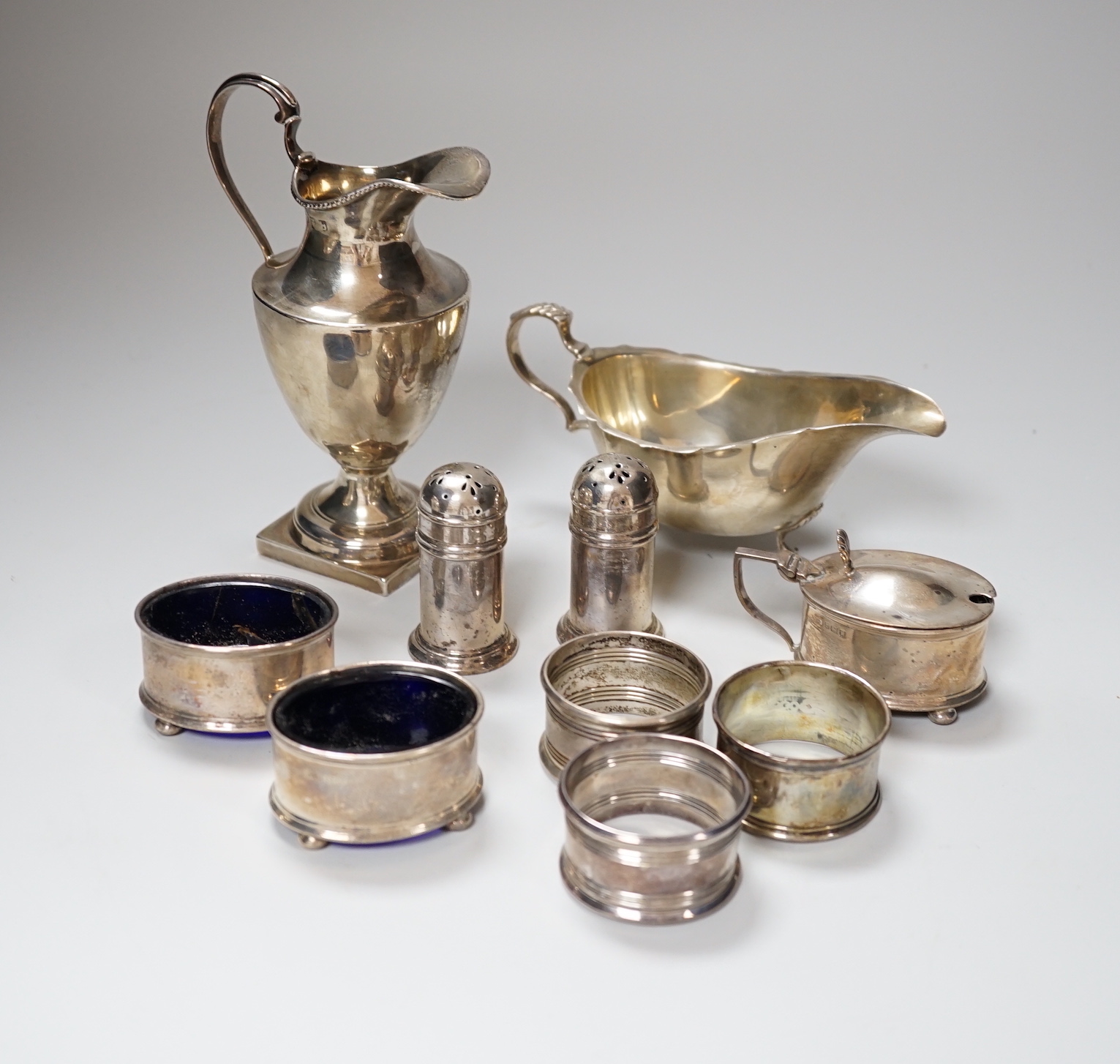 A George V silver six piece condiment set, Birmingham 1921, three odd silver napkin rings, a sauceboat, 78 grams and a cream jug, 115 grams                                                                                 