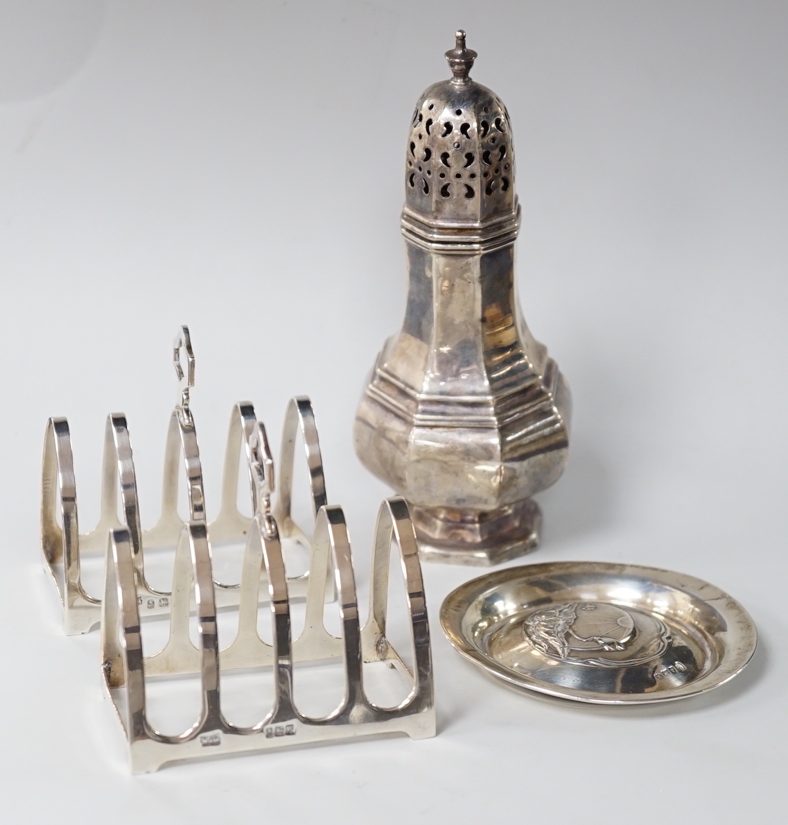 A George V octagonal silver caster, Sheffield 1932, 121 grams, a pair of Walker & Hall toast racks, Birmingham 1921, 101 grams and a trinket dish, decorated with waterlilies, Birmingham 1909, 18 grams                    